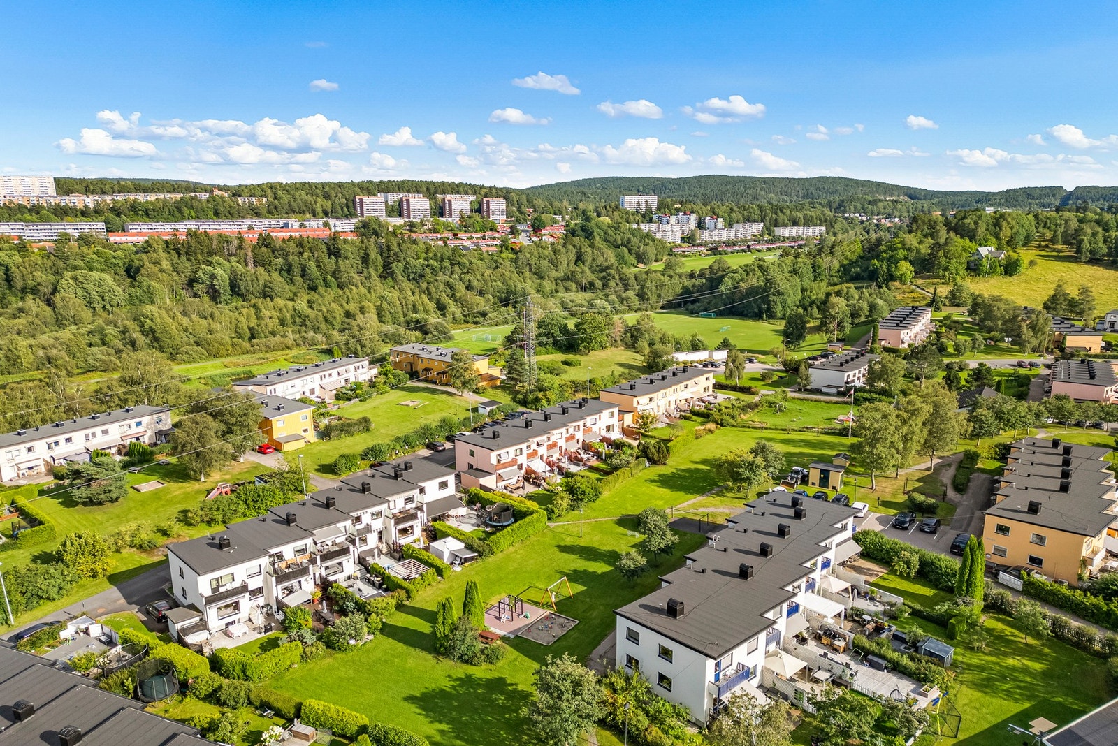 Fellestomten er pent opparbeidet med gressplen, prydbusker og trær. På tunet mellom rekkehusene er det grønne uteområder med lekeapparater og sittebenker til felles anvendelse. I bakgrunnen ruver Østmarka. Galleribilde