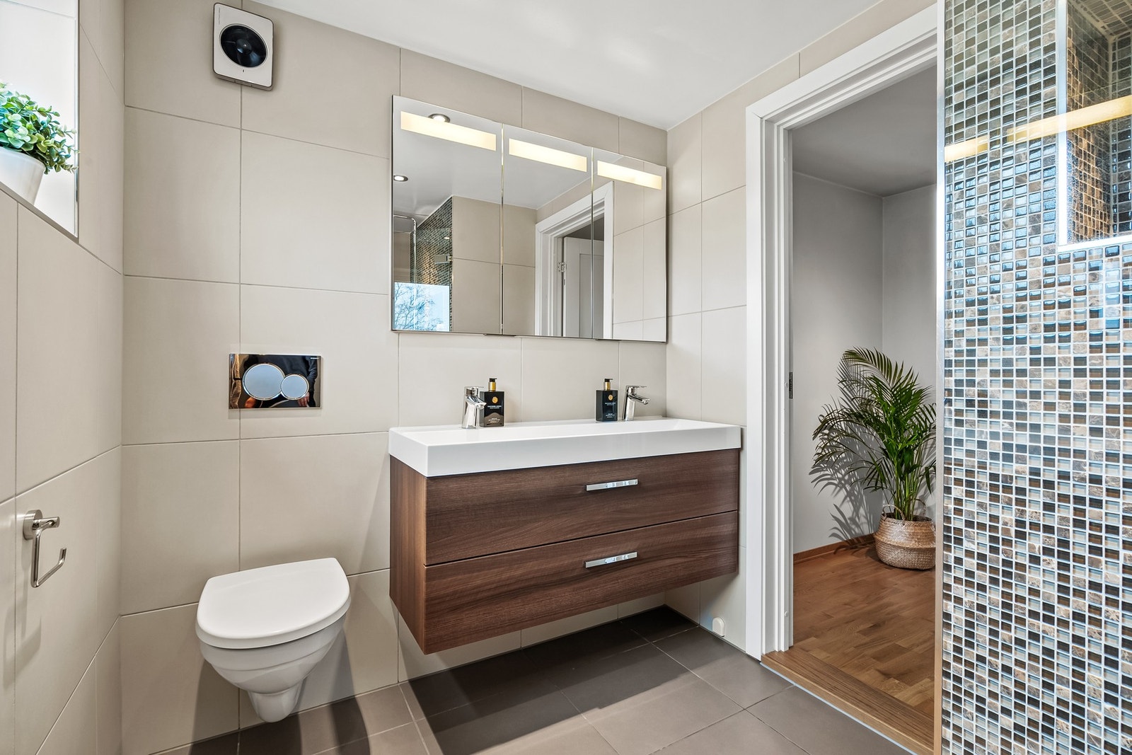 Baderomsinnredningen har mørke, finerte fronter og består av en heldekkende servant på en skuffeseksjon og et bredt speilskap med belysning. Galleribilde