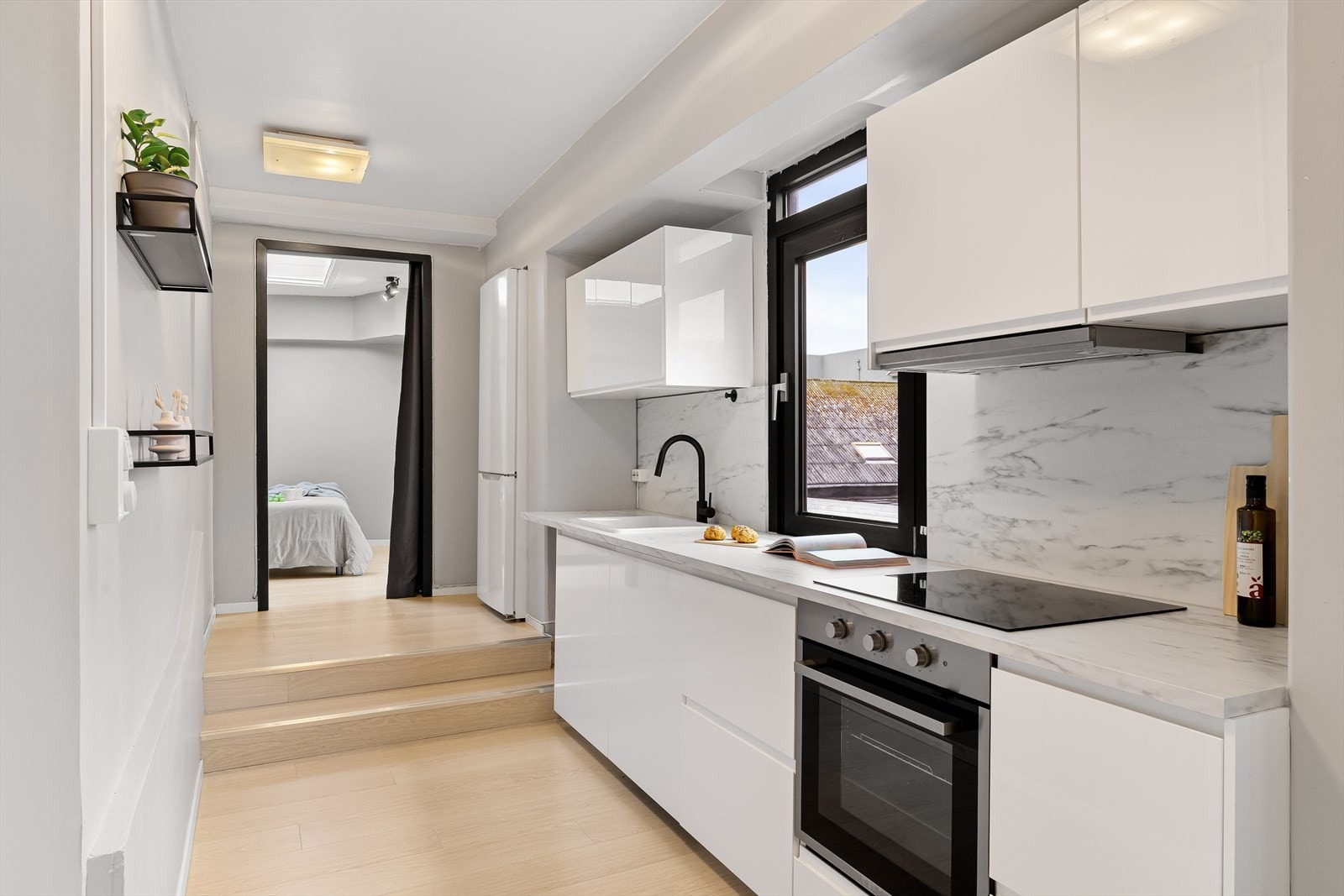 Hvite fronter med innfelte håndtak og integrerte hvitevarer som stekeovn, platetopp og oppvaskmaskin. Plass til frittstående kjøleskap. Galleribilde