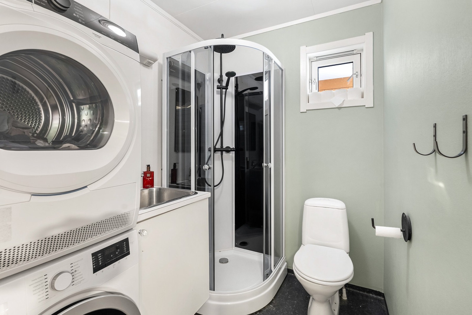 Bad/vaskerom med våtromstapet/belegg på veggene og vinylbelegg på gulvet. Innredning med toalett, dusjkabinett, opplegg for vaskemaskin og skyllekar i benk. Galleribilde