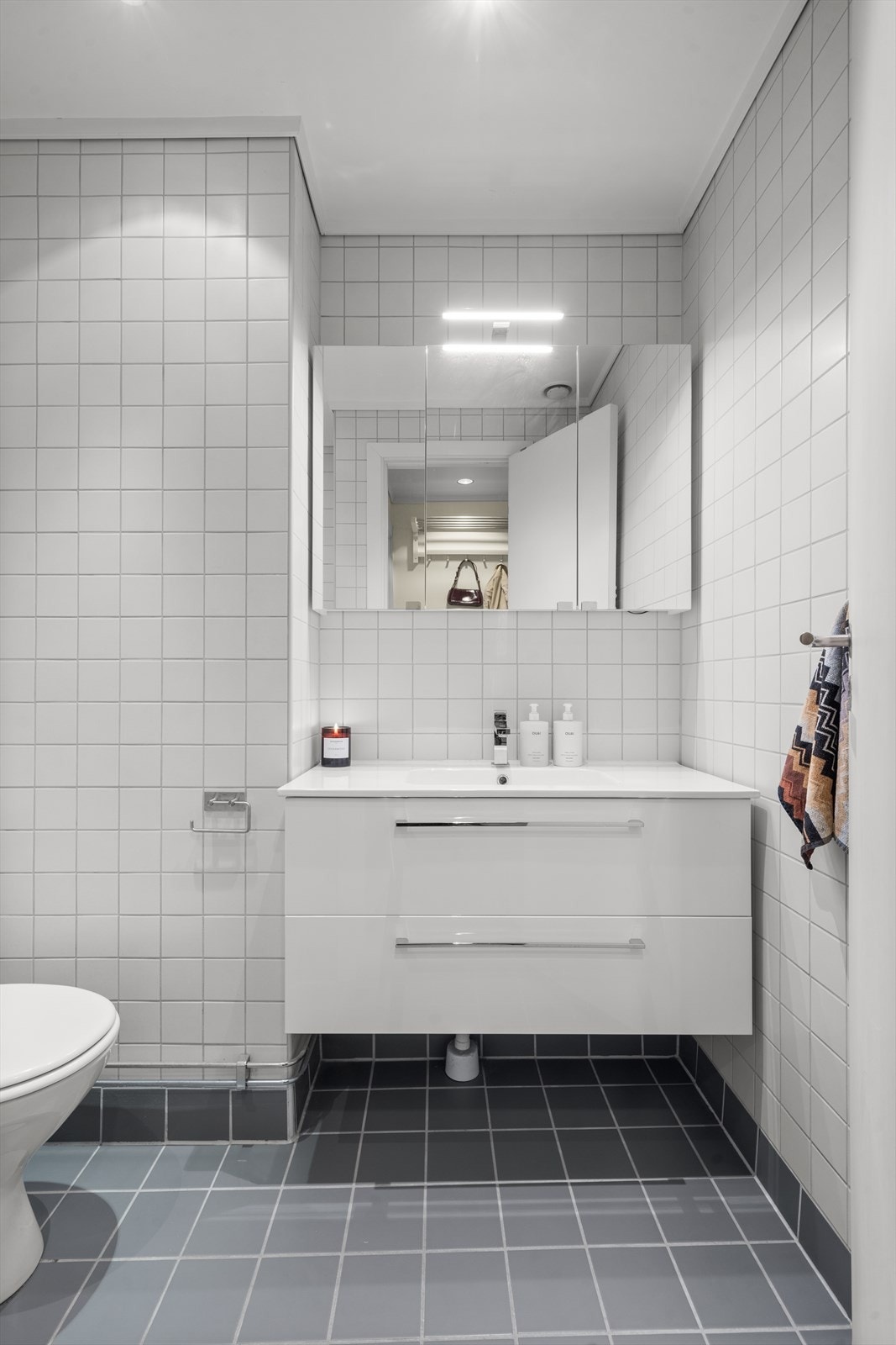 Moderne bad med flislagte vegger og gulv, gulvvarme, og lys innredning med glatte fronter. Galleribilde