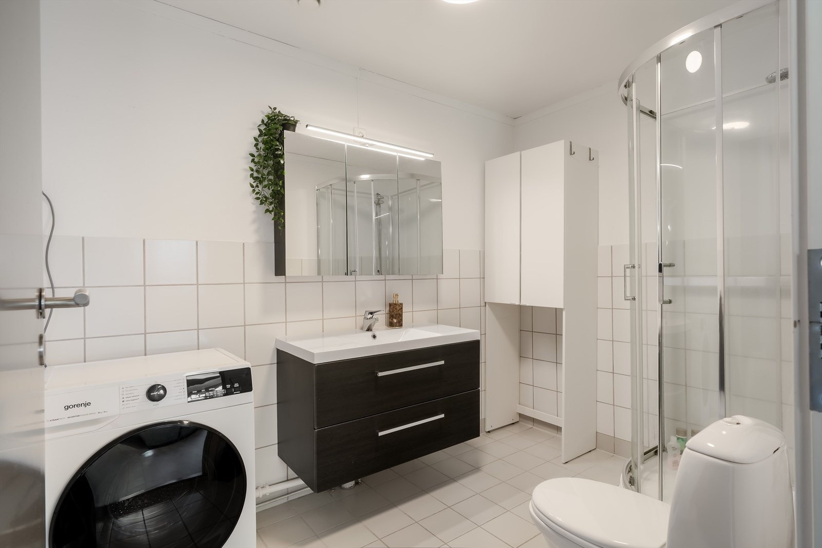 Stort, flislagt bad med dusjkabinett og opplegg for vaskemaskin. Galleribilde