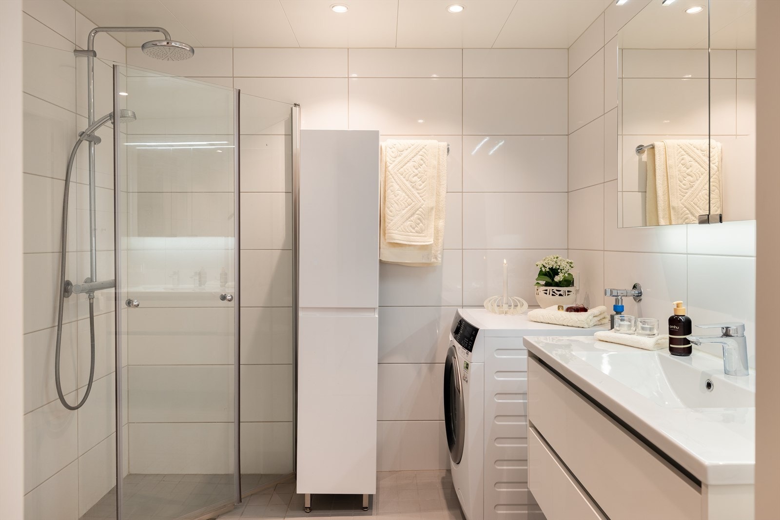 Badet er utstyrt med dusjdører, servant i skap, vegghengt toalett og opplegg for vaskemaskin. Galleribilde