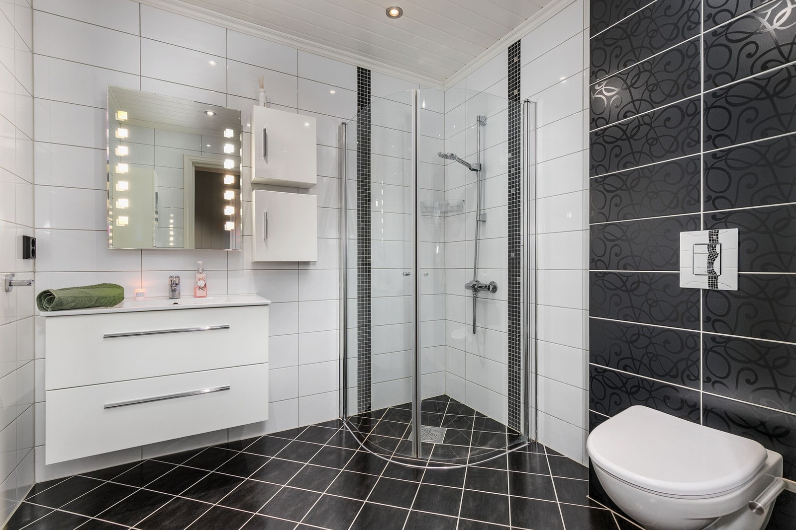 Badet har dusjkabinett, vegghengt toalett, servant med skuffer og speil med innebygd belysning. Galleribilde