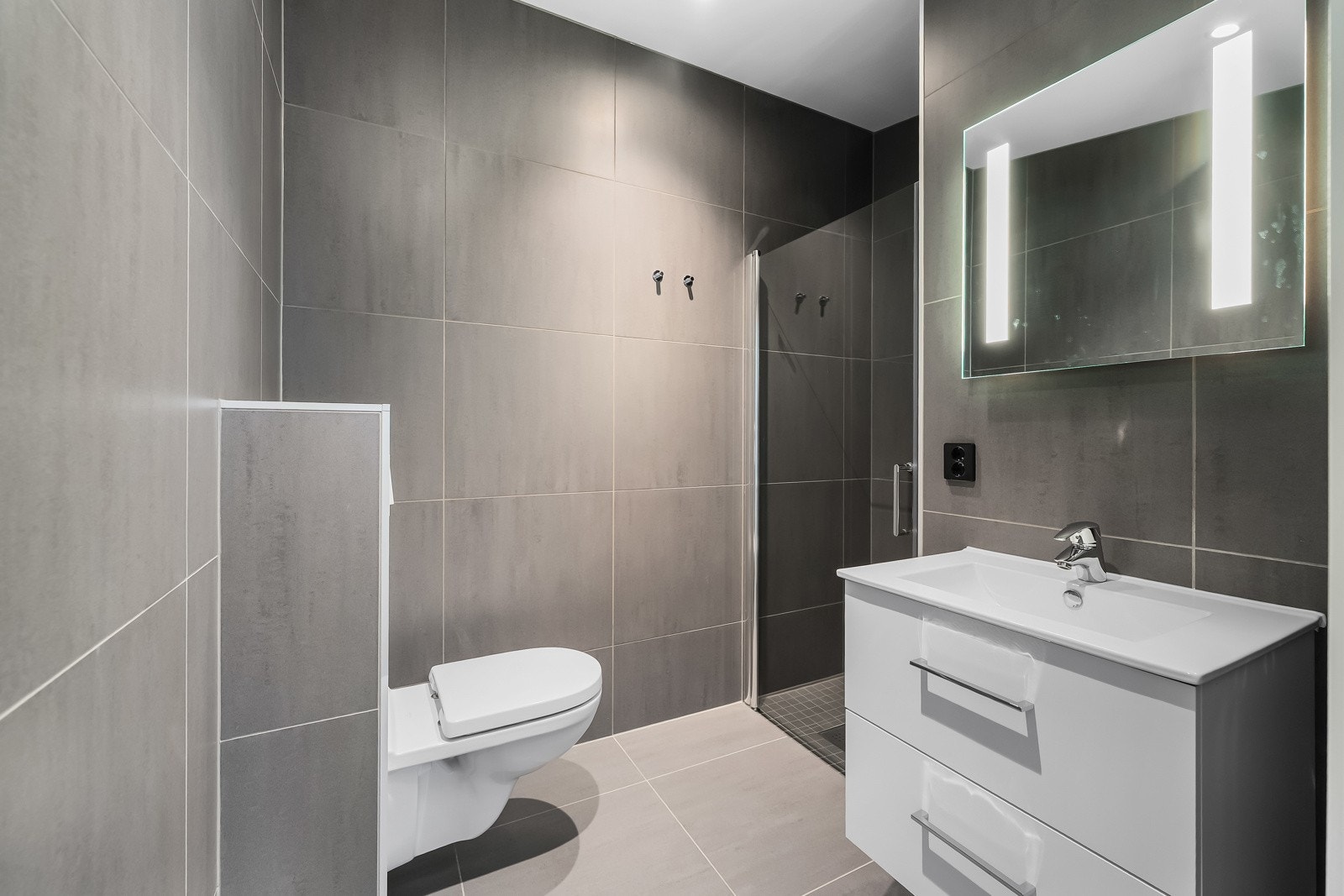 Delikat flislagt bad m/gulvvarme i boligens loftetasje, i tillegg til smakfulle storformatfliser på vegger og gulv i tidsriktig farge. Innredningen består av stilrent servantmøblement med skuffer, speil, vegghengt toalett. Galleribilde