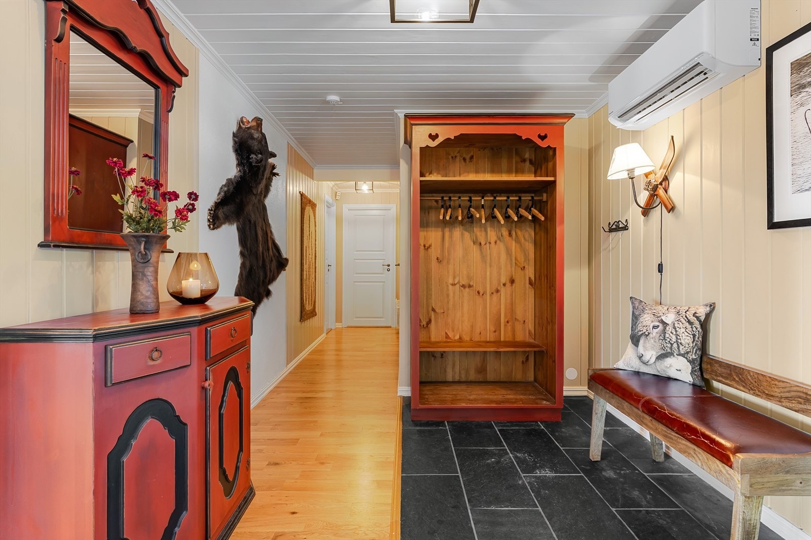 Inne i hytta møtes du av en romslig gang med god plass til garderobeløsninger. Her er det også installert varmepumpe. Det gjøres oppmerksom på at den vegghengte lampen ikke medfølger salget. Galleribilde