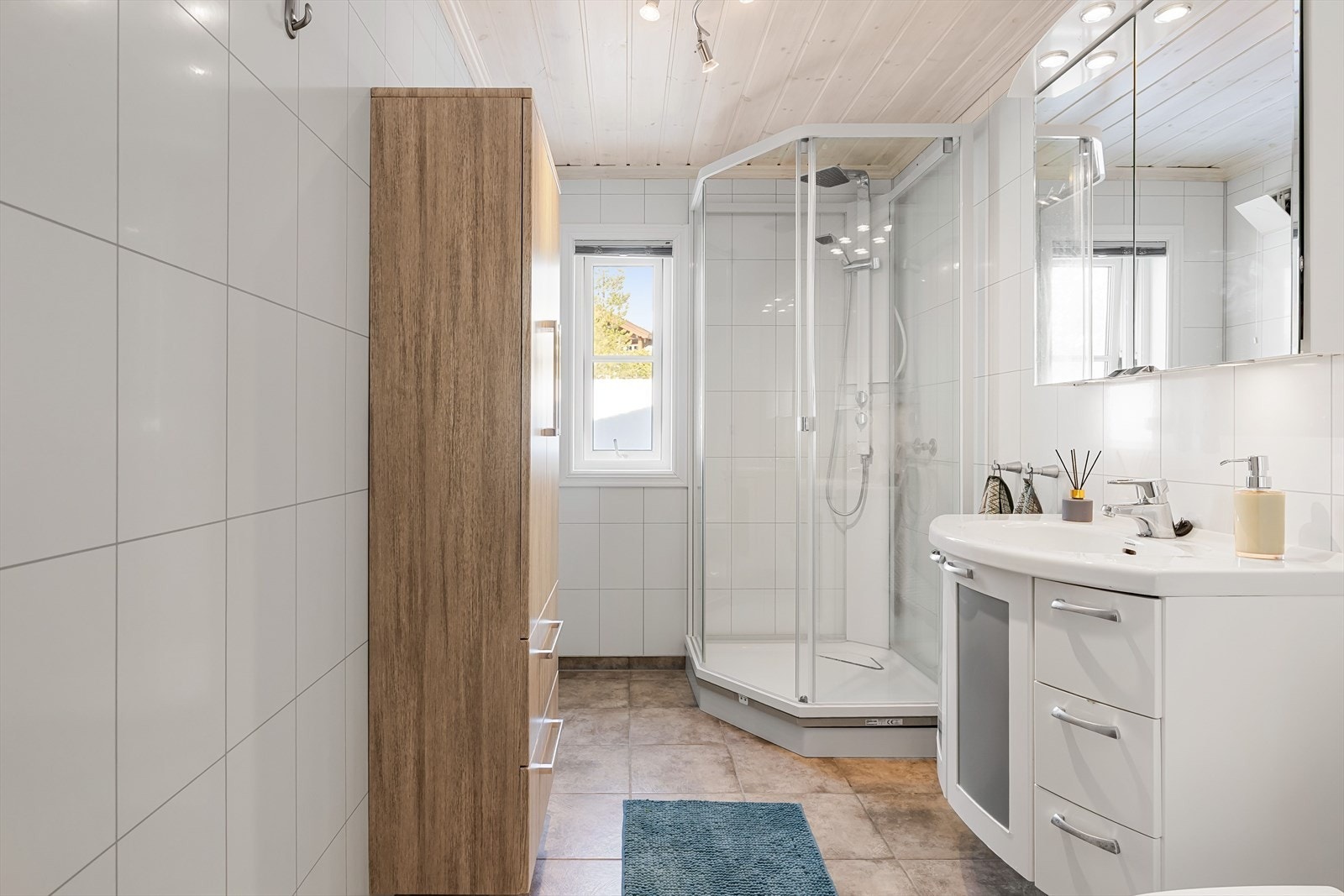 Pent baderom med varmekabler i gulvet. Baderommet er innredet med servant på innredning, dusjkabinett og skap med speil og belysning. Galleribilde