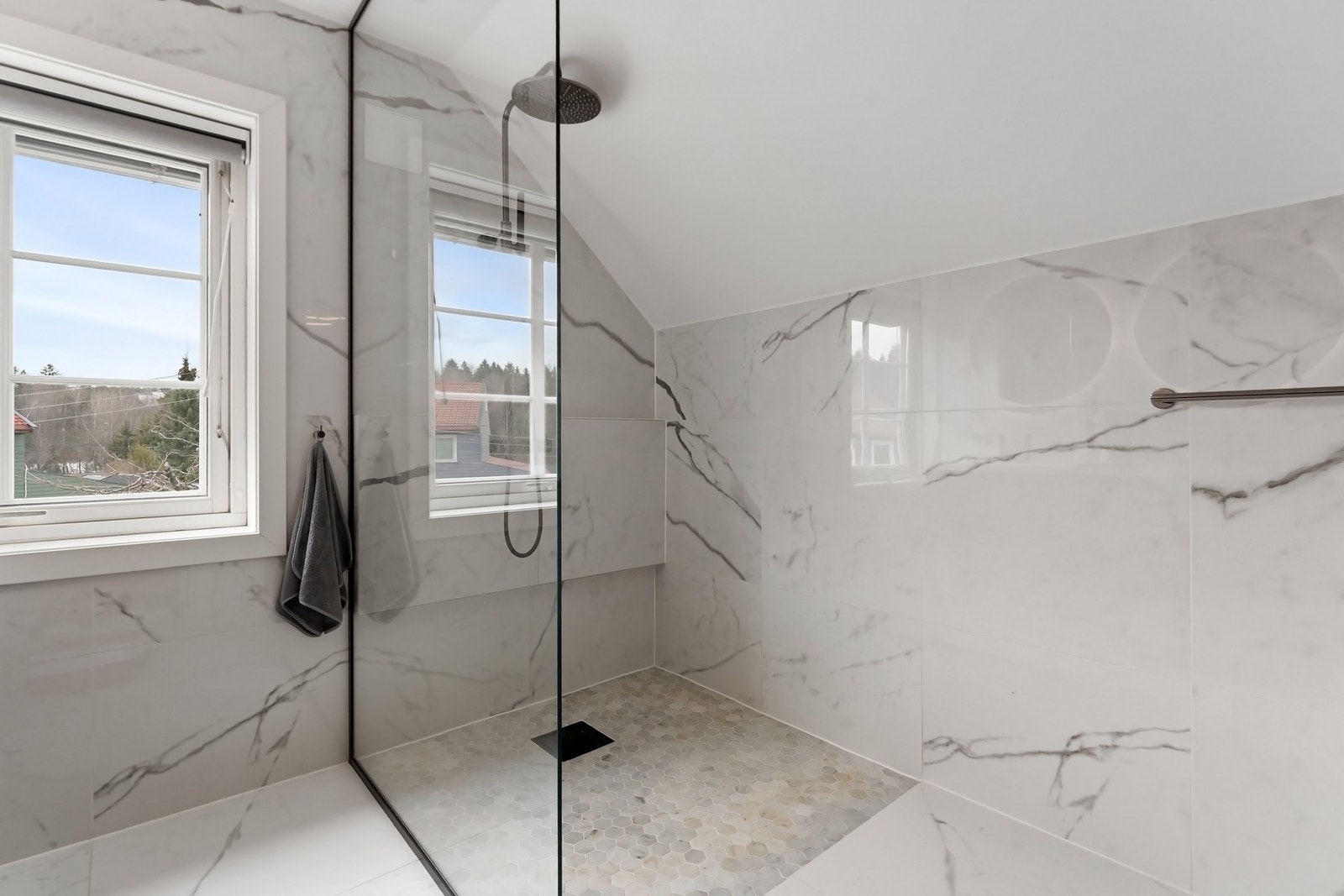 Vegger og gulv er kledd i lyse, marmorerte fliser, kombinert med lys heksagonmosaikk på gulvet i dusjsonen. Galleribilde