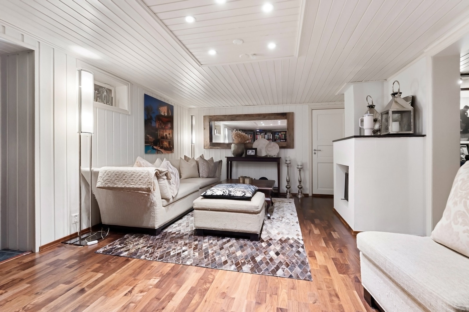 Kjellerstuen har hygge fra en peis med glassdører, pusset, hvitmalt mur og sort peishylle. Galleribilde