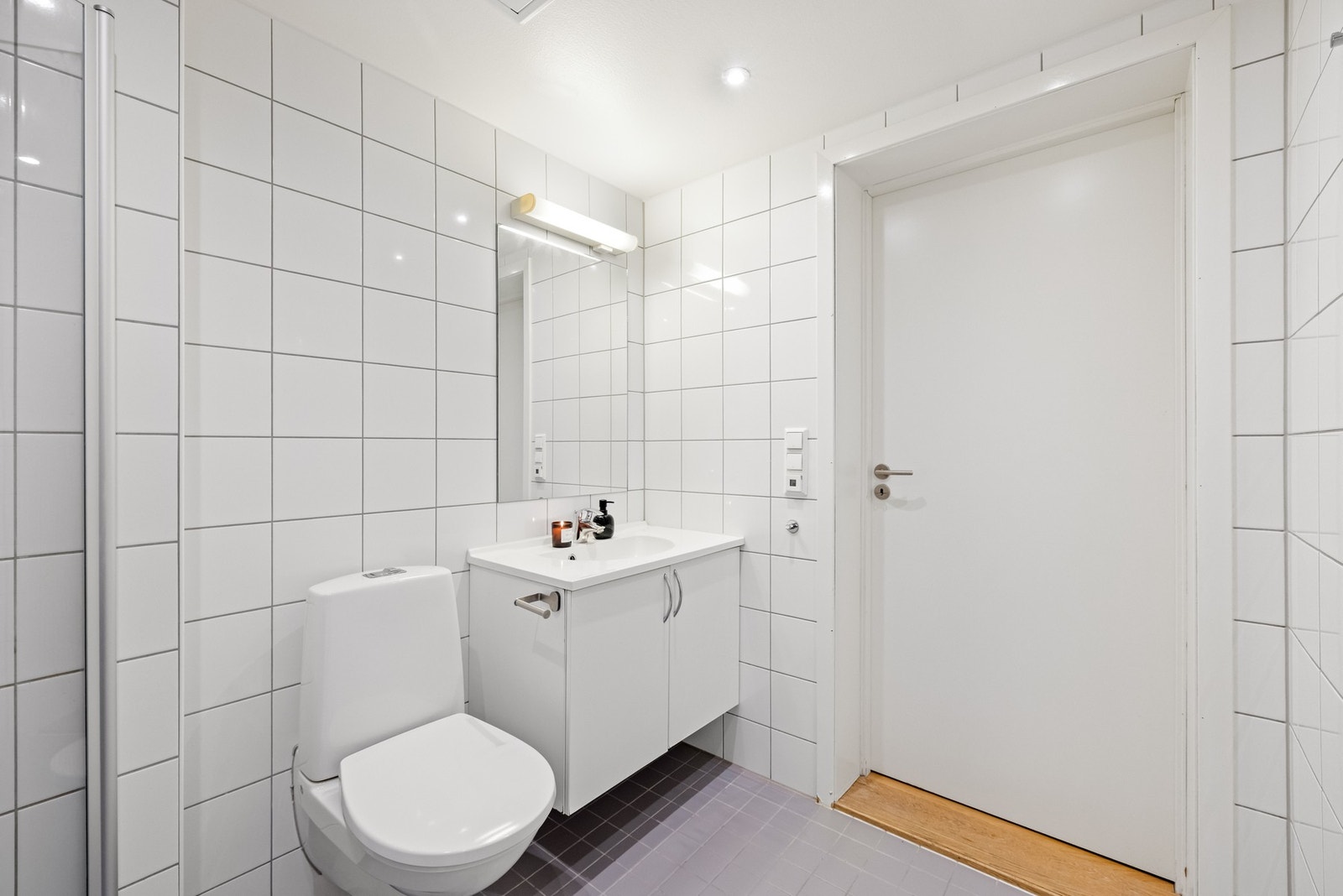 Rommet er innredet med servant med tilhørende benkeskap, speil og belysning over servant, dusjsone med innfellbare glassdører og vegghengt toalett med innkasset sisterne. Galleribilde