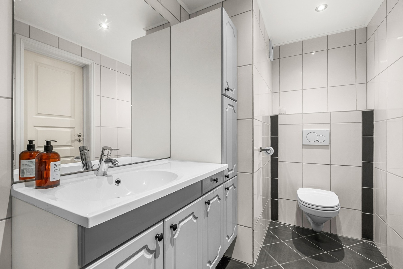 Badet er innredet med veggmontert toalett, servant og skapinnredning, dusjkabinett og opplegg for vaskemaskin Galleribilde