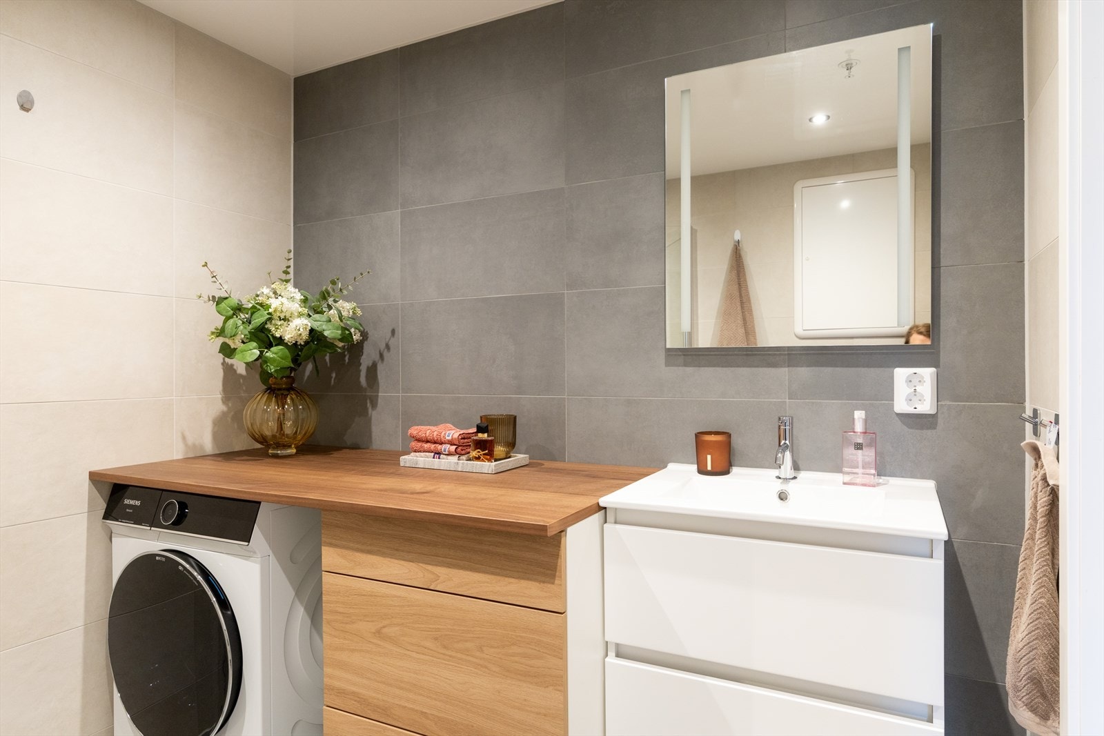 Badet er innredet med vegghengt klosett, servant med innredning, speil med lys og dusjhjørne med svingbare glassdører. Galleribilde