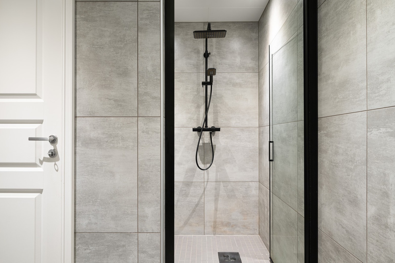 Badet inneholder vegghengt toalett, helstøpt servant, skuffer under servant med slette fronter og dusjdører i klart glass. Galleribilde