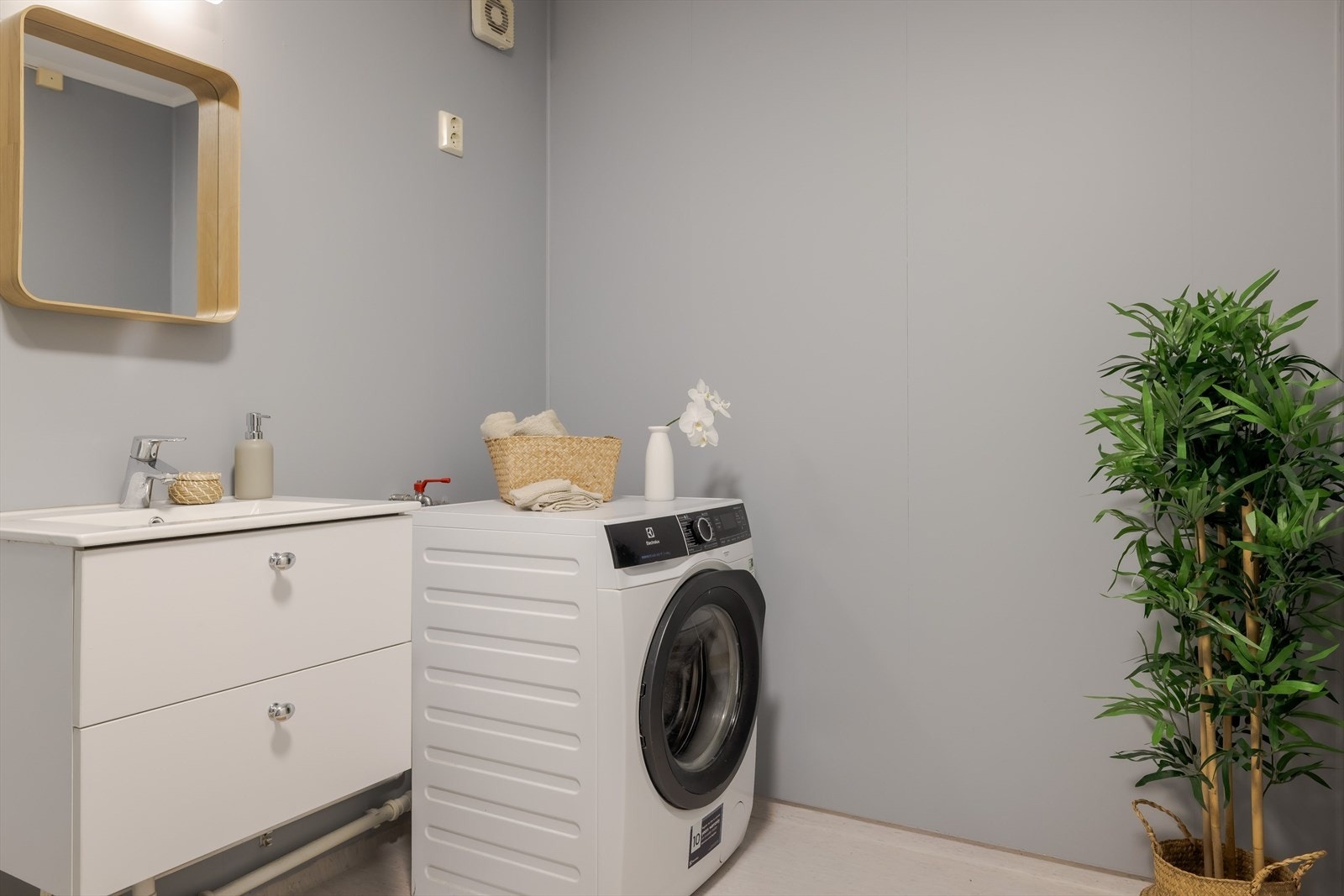 Lys baderomsinnredning med skuffer og heldekkende servant. I hjørnet er det plass og opplegg for vaskemaskin, samt tørketrommel over om ønskelig. Galleribilde