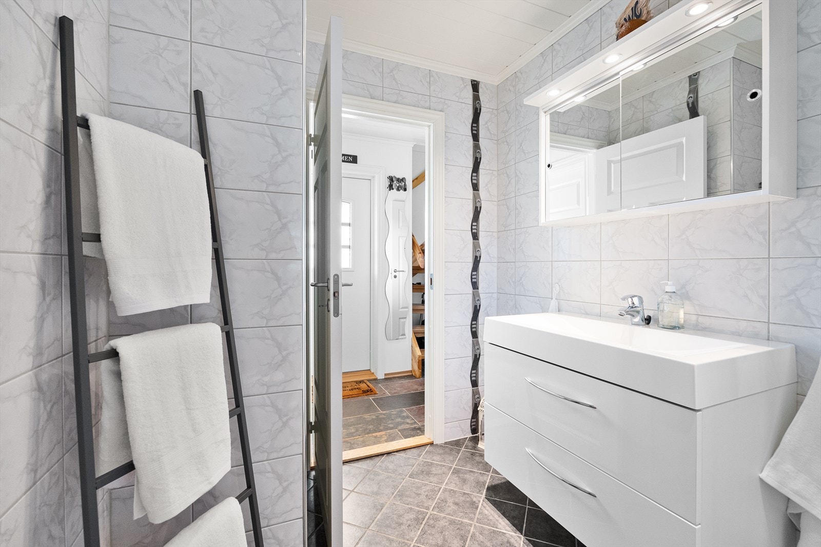 Badet er innredet med dusjhjørne, vegghengt toalett, benkeskap med nedfelt servant og speil med belysning over. Galleribilde