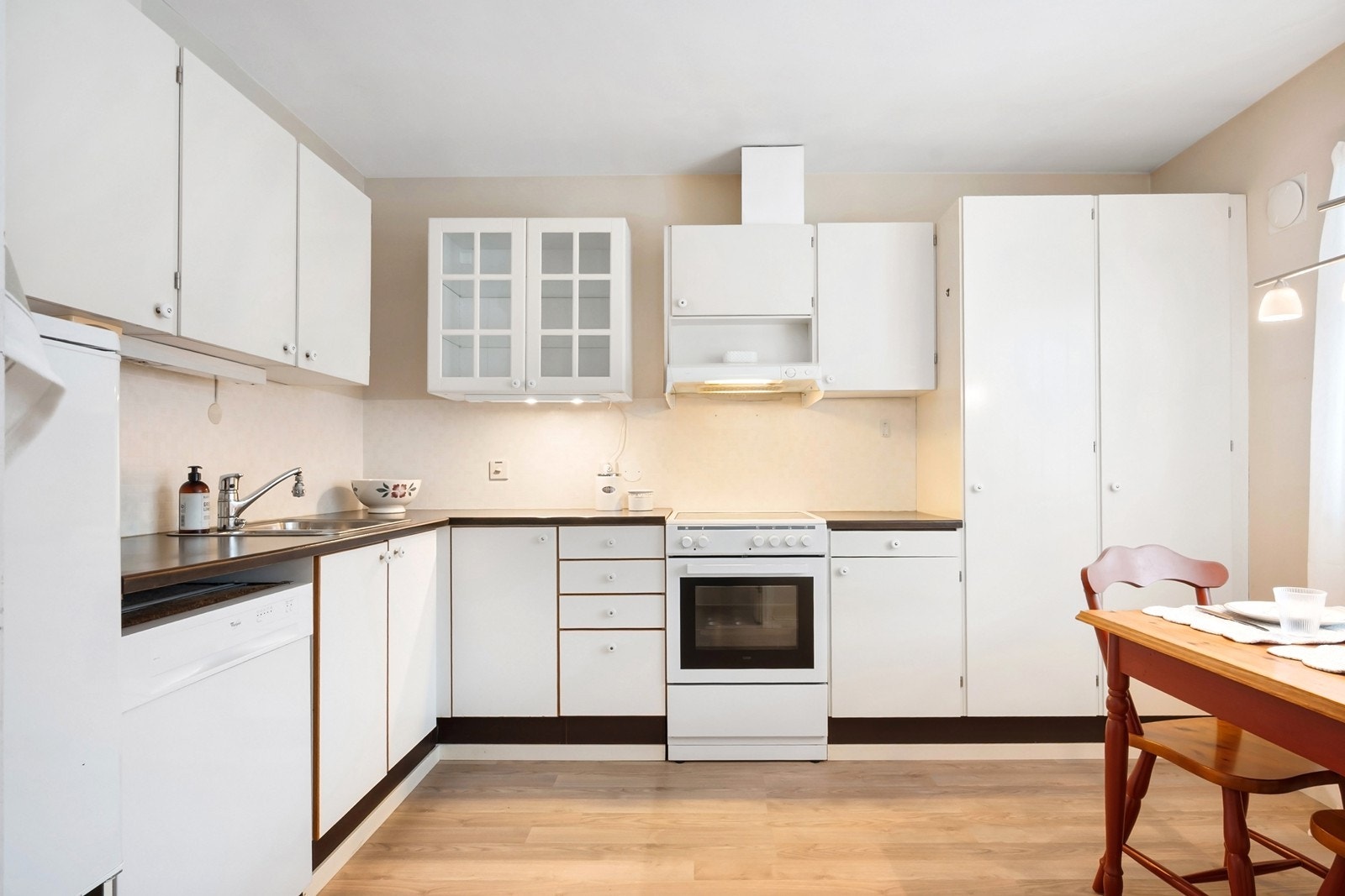 Kjøkkenet ligger i adskilt rom med innredning i en praktisk L-form og plass til spisebord. Over- og underskap med rettprofilerte fronter gir god oppbevaring, mens laminat benkeplate sørger for gode arbeidsflater Galleribilde