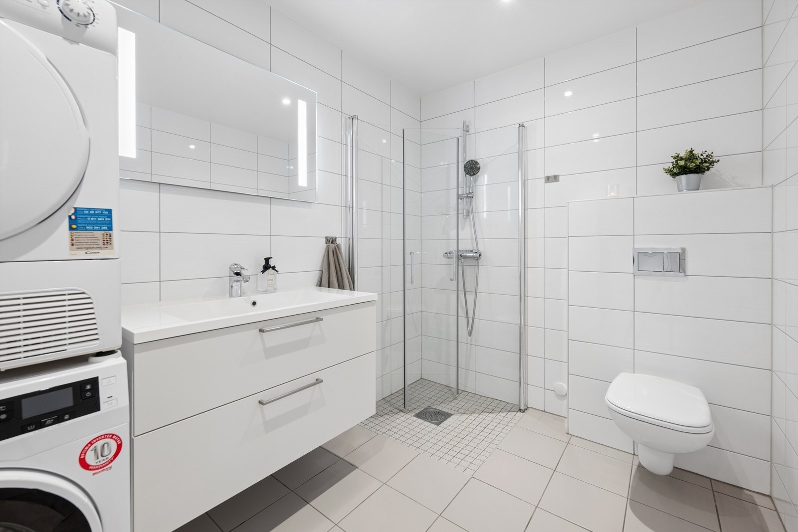 Lekkert, flislagt bad fra byggeår. Rommet er innredet med dusjhjørne med glassvegger, vegghengt toalett, innredning med servant og opplegg for vaskemaskin. Galleribilde