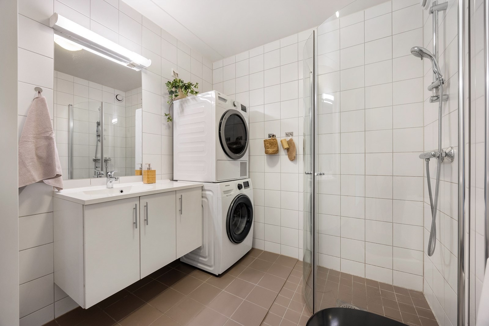 Flislagt bad med varmekabler i gulvet, nedsenket dusjhjørne med glassdører og opplegg for vaskemaskin. Galleribilde