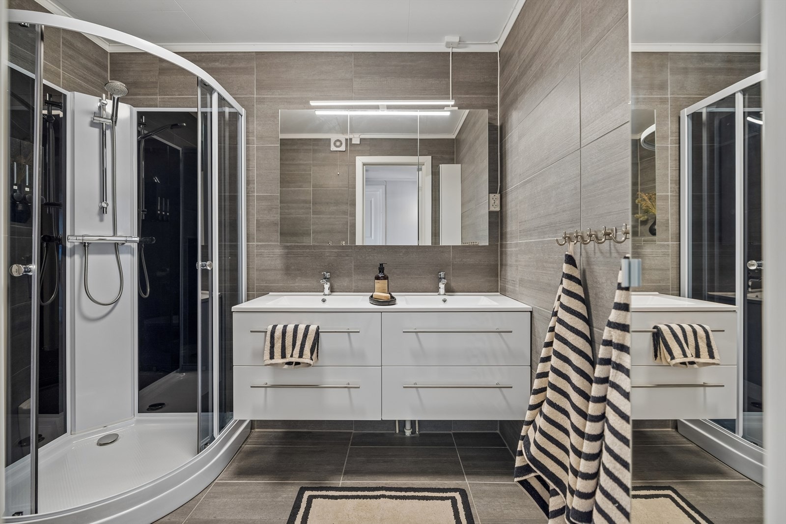 Bad med flislagte overflater, dusjløsning og baderomsinnredning med servant. Galleribilde