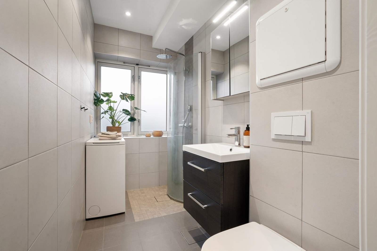 Badet er innredet med baderomsinnredning med nedfelt servant, veggmontert toalett og dusjhjørne med dusjvegger. Galleribilde