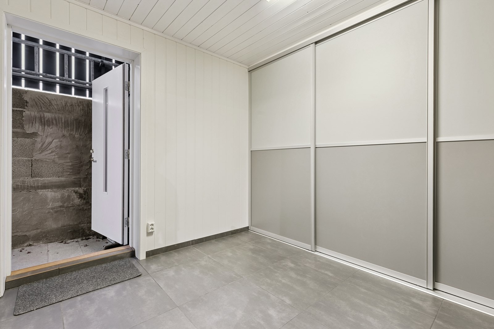 Nedgang fra gårdsplassen til en romslig grovinngang. Rommet er pusset opp med pene fliser på gulv og en stor skyvedørsgarderobe. Galleribilde