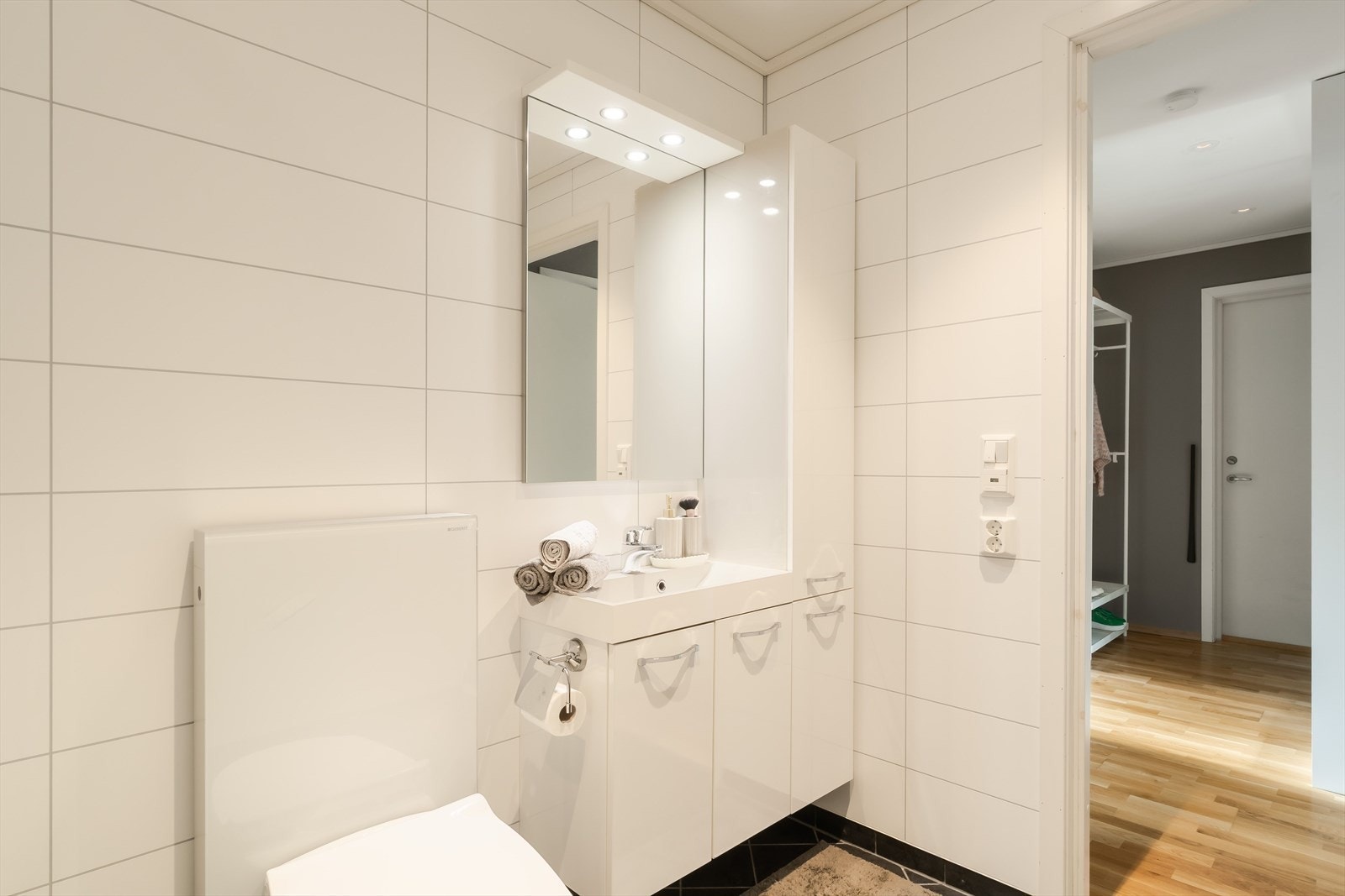 Badet er innredet med en moderne servant, praktiske hyller og et dusjkabinett. Gulvvarme bidrar til en lun og behagelig temperatur året rundt. Galleribilde