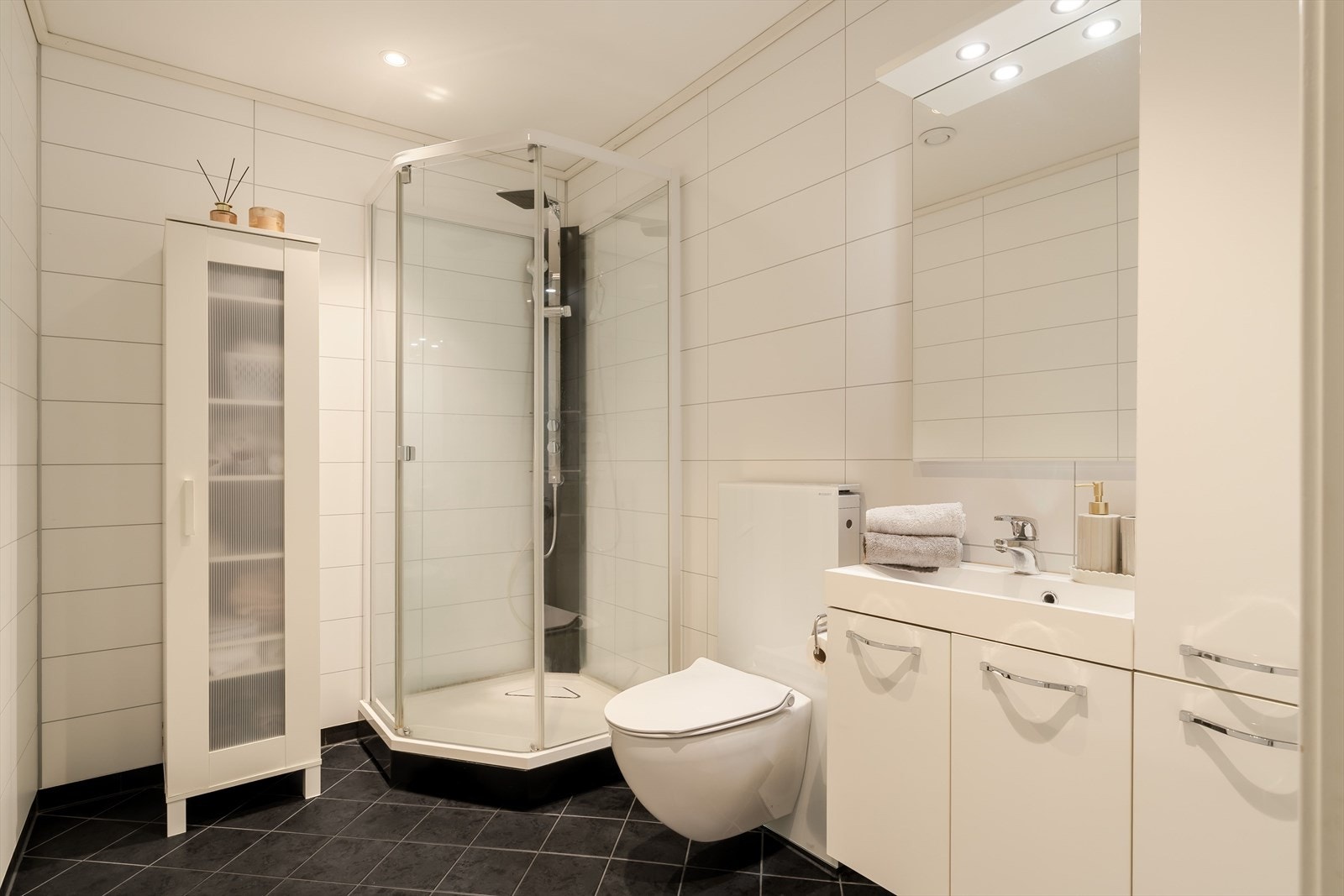 Baderommet er tidsriktig og stilrent med mørke fliser på gulvet og baderomsplater med flisprofil på veggene. Galleribilde