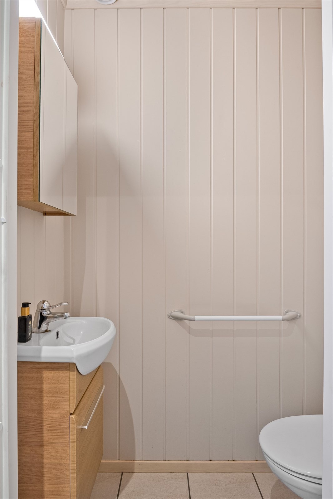 Praktisk ekstra toalettrom med flislagt gulv og vannbåren gulvvarme. Toalettrommet er utstyrt med pent servantskap, speilskap med belysning over og toalett. Galleribilde