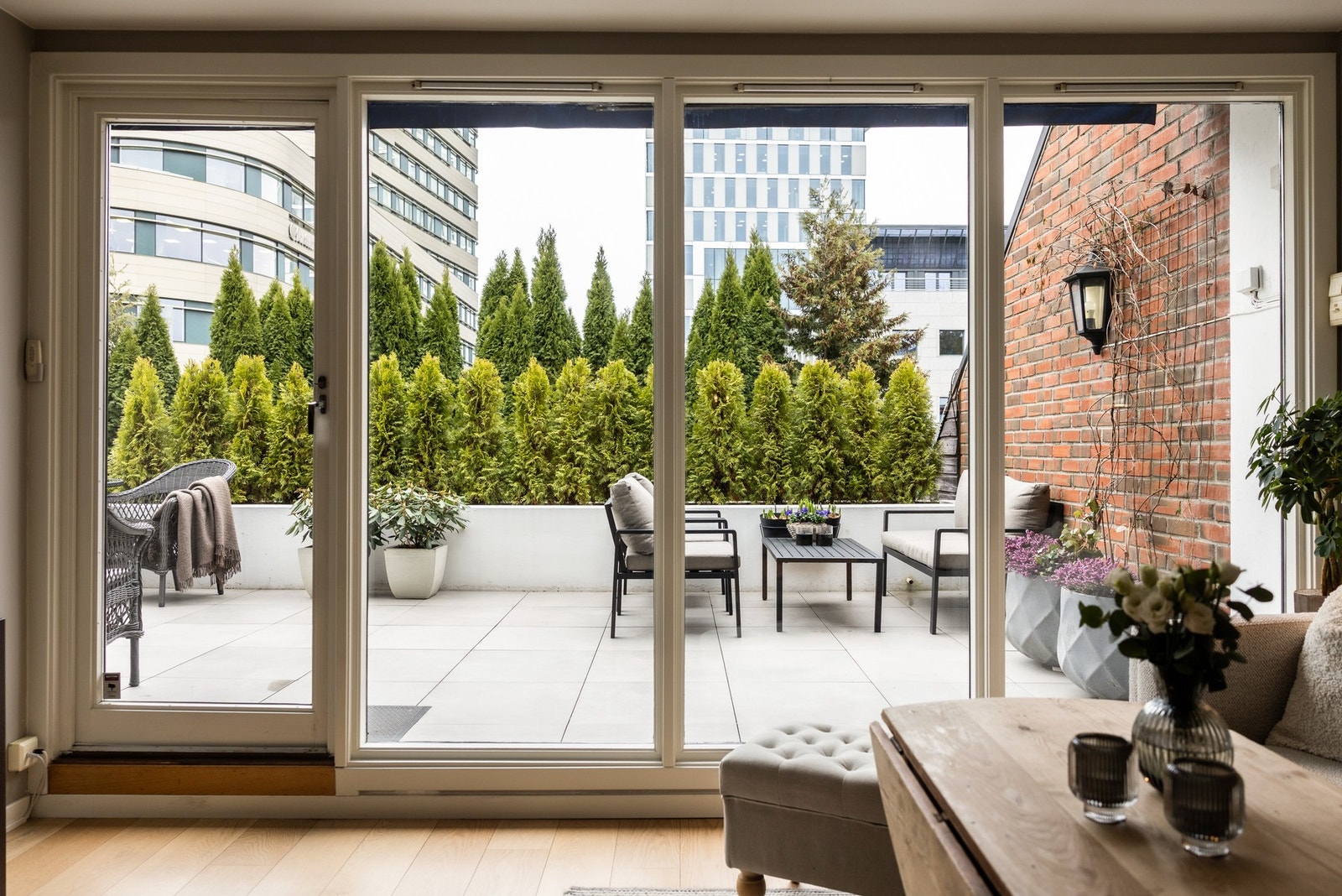 Terrasse med utsikt over moderne bygninger, skjermet av tett grønn vegetasjon gir privatliv. Galleribilde