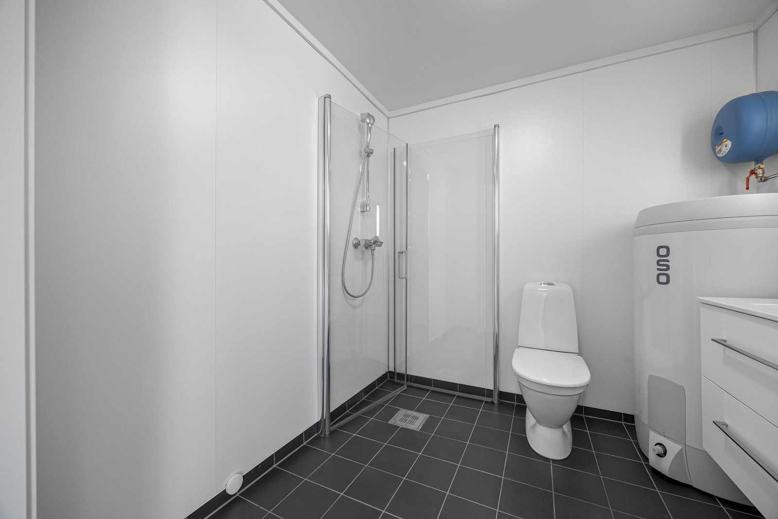 Baderom med opplegg til vaskemaskin, dusjhjørne, toalett, varmtvannsbereder (200l) og servant med speil og skuffer. Galleribilde