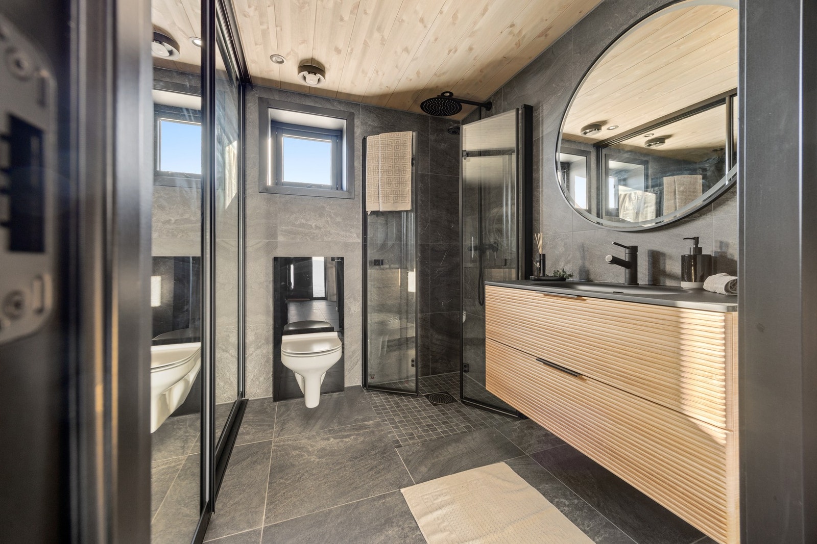 Badet er holdt i delikate flis- og materialvalg. Downlights. Varmtvannsbereder og opplegg for vaskemaskin er gjemt bak skyvedør. Galleribilde