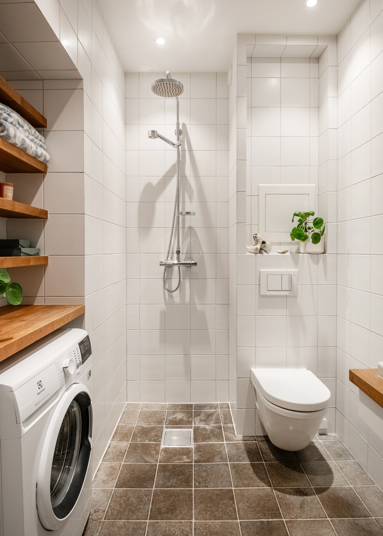 Flislagt baderom med dusjnisje, vegghengt toalett og varmekabler i gulv. Opplegg for vaskemaskin under hyllenisje Galleribilde