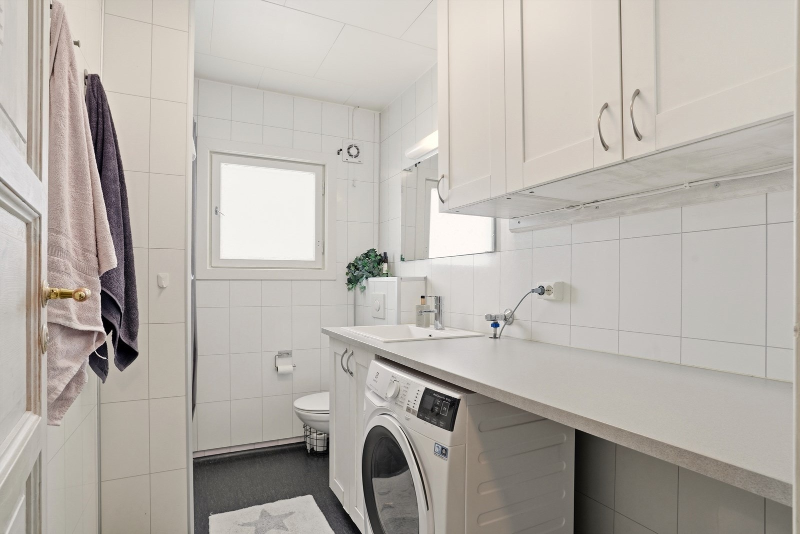 Badet har belegg på gulv og baderomsplater på vegger. Opplegg og plass til vaskemaskin og tørketrommel. Galleribilde