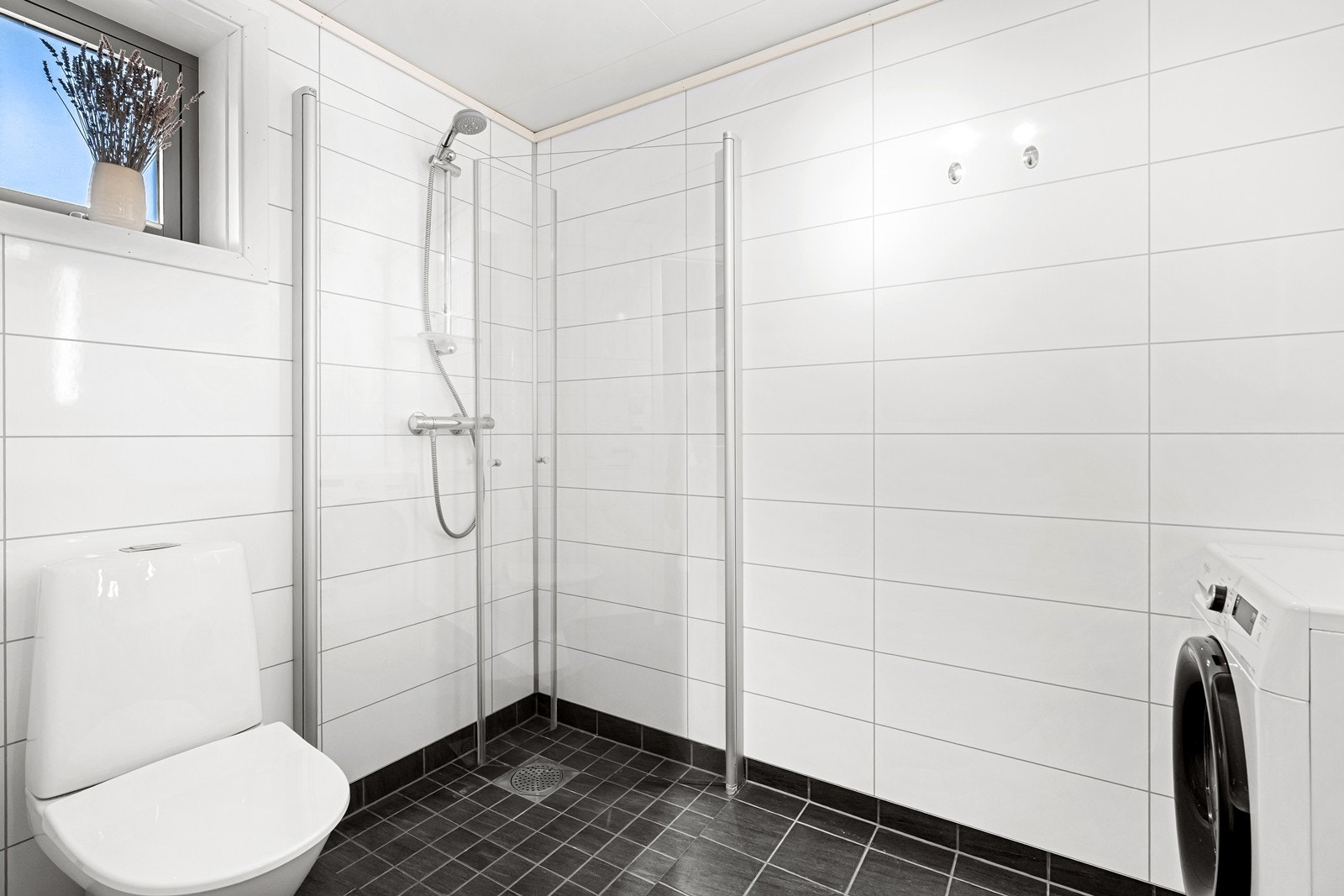 Badet er i klassiske farger med hvite våtromsplater på veggene, og mørke fliser på gulv. Galleribilde