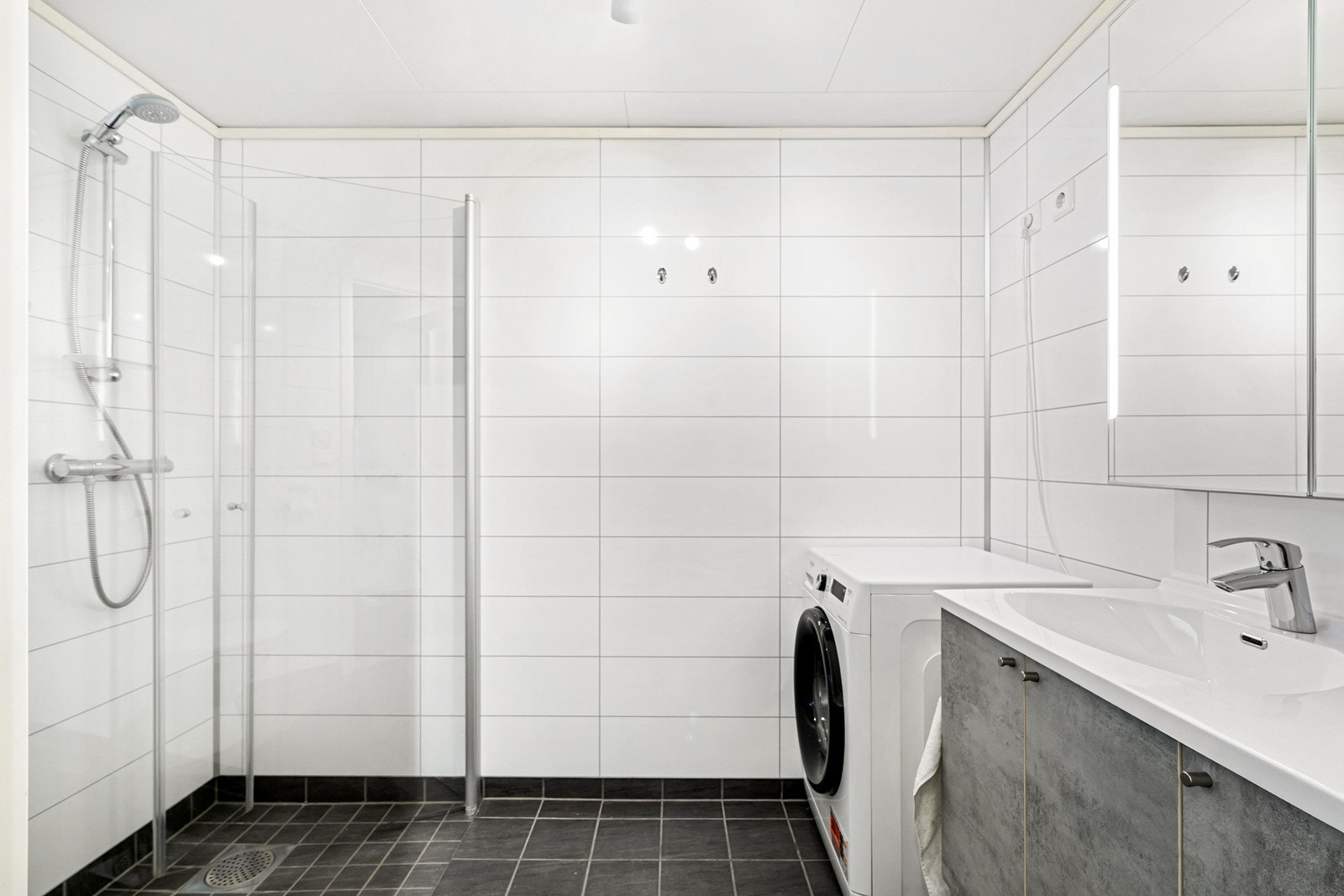 Innredet med dusjhørne, toalett, servant med skap og speil med oppbevaringsmuligheter. Badet har også opplegg for vaskemaskin Galleribilde