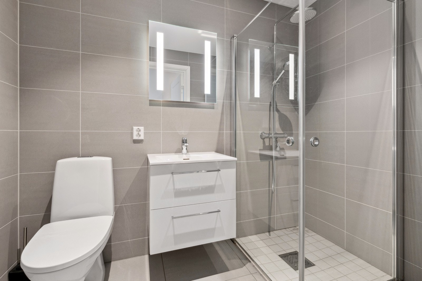 Pent bad nr. 2 med flislagte overflater og varmekabler i gulv. Innredningen består av stilrent servantmøblement, speil m/integrert belysning, toalett og separat dusjhjørne. Galleribilde