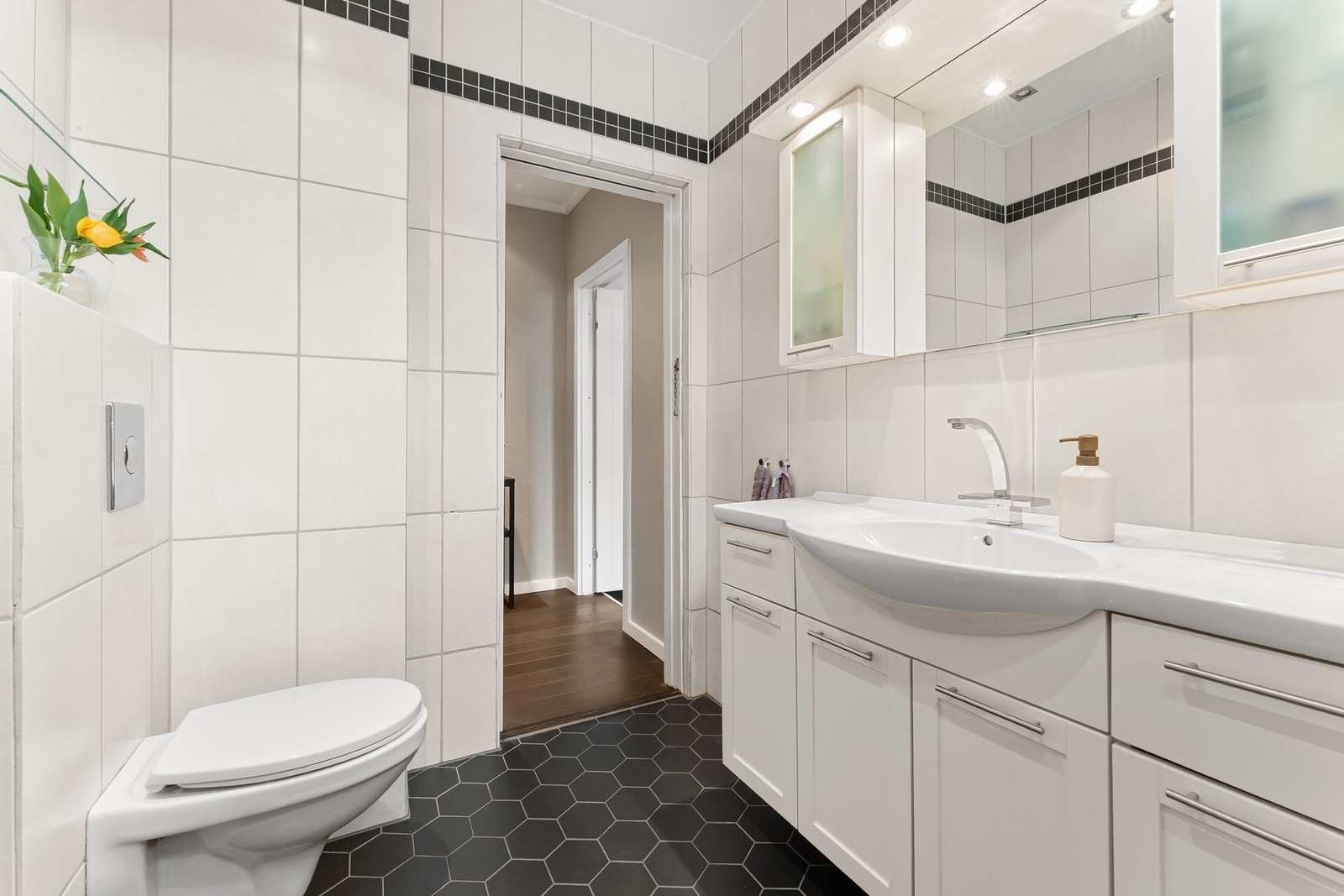 Badet har delikat innredning med flislagte vegger og gulv. Videre er det vegghengt toalett, servantskap med praktisk oppbevaringsmulighet. Galleribilde