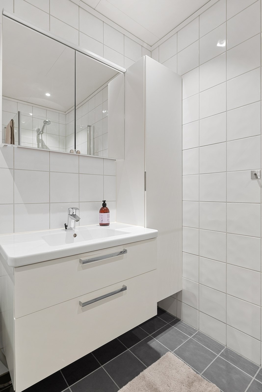 Badet har en moderne baderomsinnredning bestående av servantskap, høyskap og speilskap, som gir rikelig med oppbevaringsplass. Galleribilde