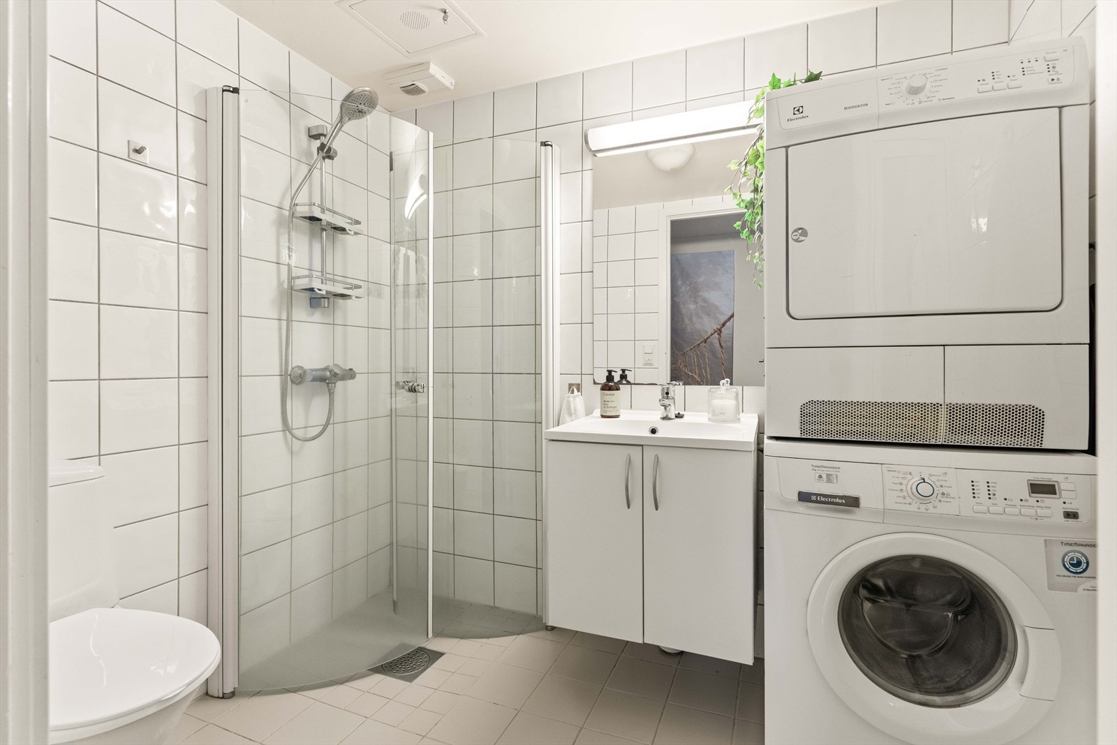 Flislagt bad med dusjhjørne og praktisk opplegg for vaskemaskin og tørketrommel. Et funksjonelt rom med god plass. Galleribilde