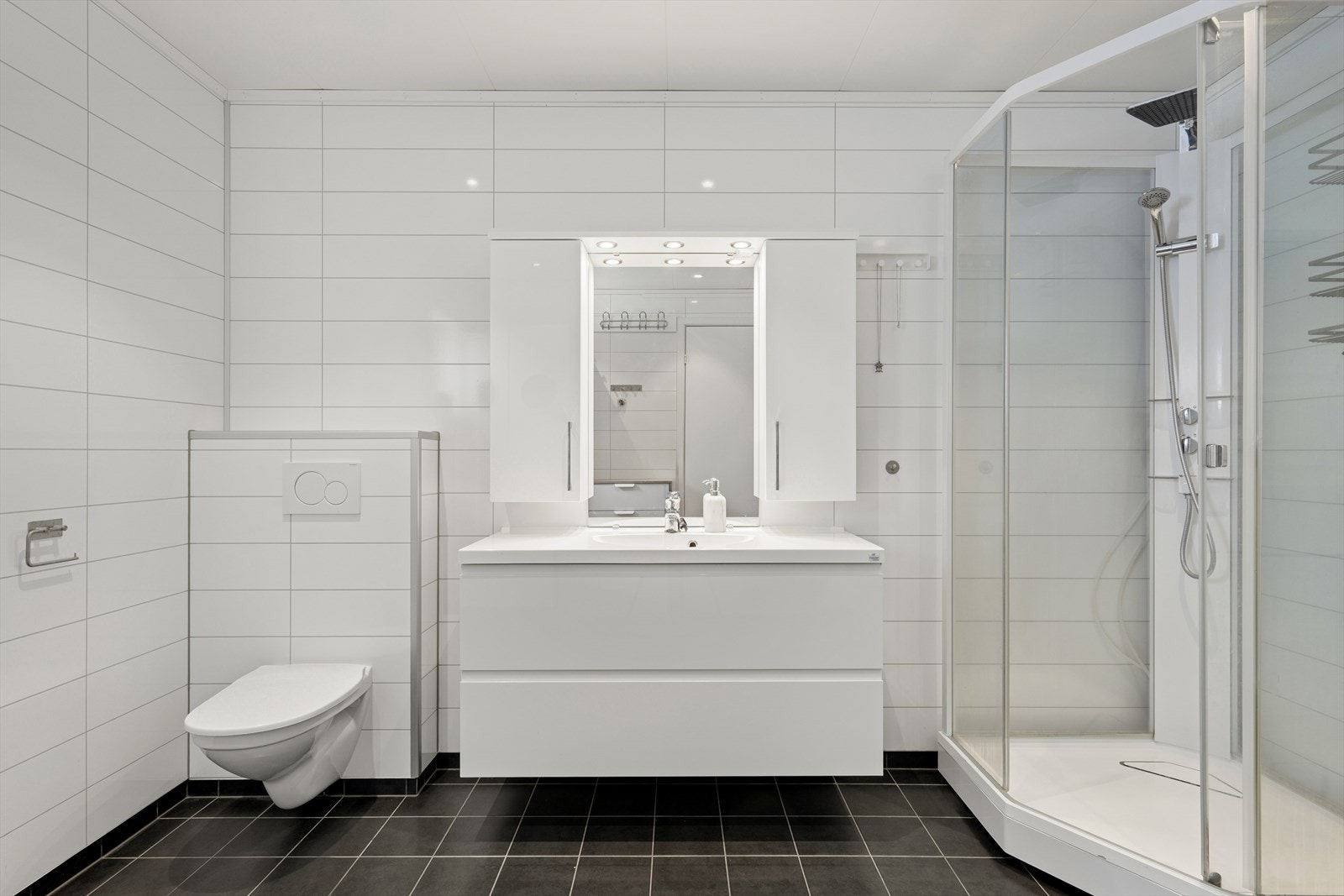 Innredningen består av vegghengt speil, overskap med lys, servant med seksjon, vegghengt toalett, dusjkabinett og opplegg for vaskemaskin. Galleribilde