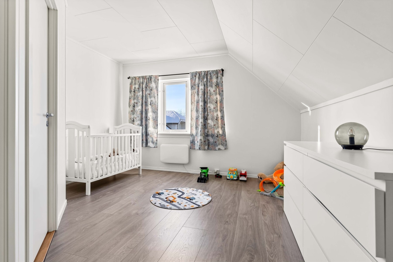 Soverom 2 fremstår som et koselig soverom med malte slette veggflater, laminat på gulv og et stort vindu. Galleribilde