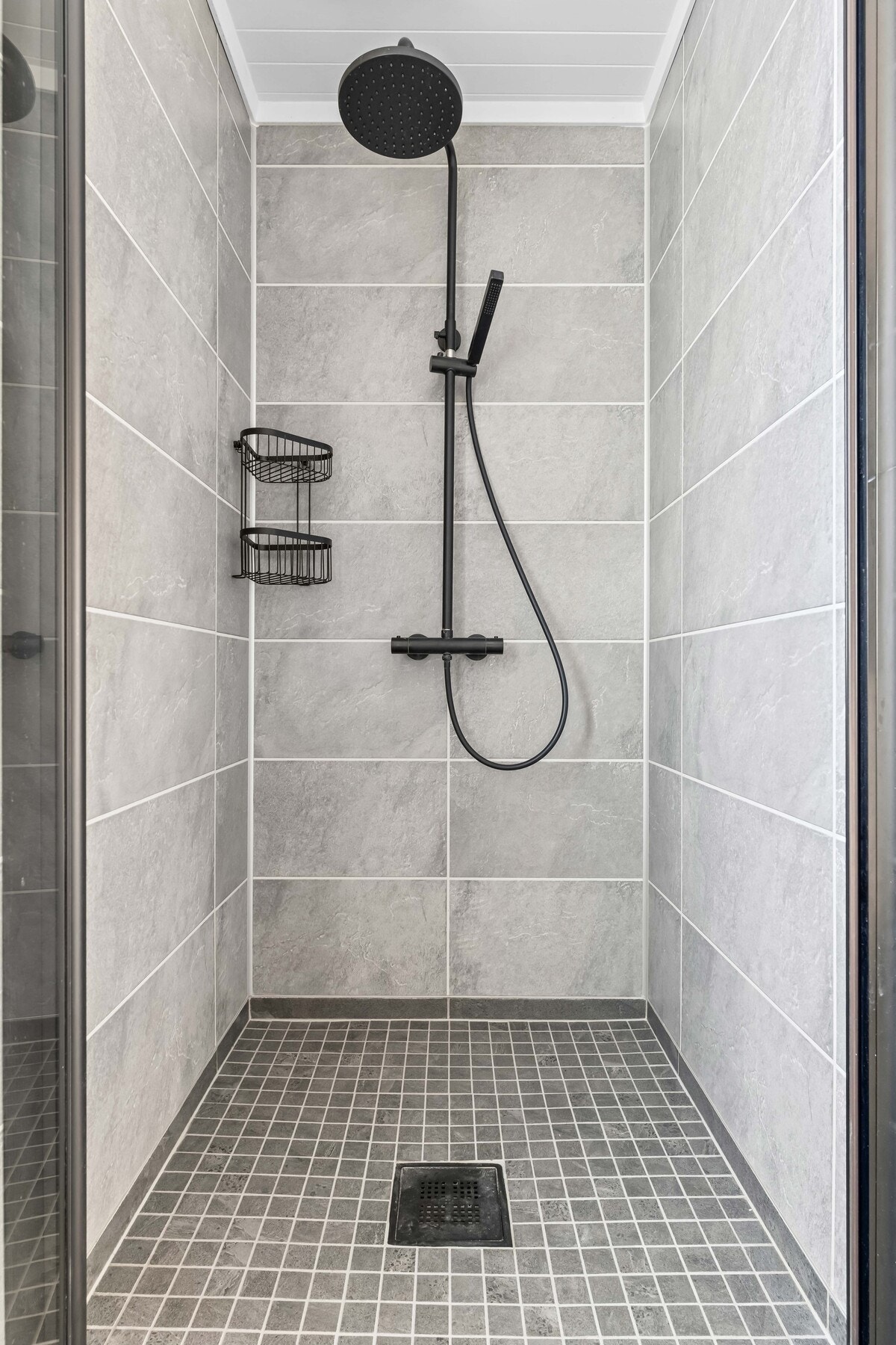 Separat dusjnisje med regnfallsdusj og glassvegg. Omramminger og armaturer i sort design. Galleribilde