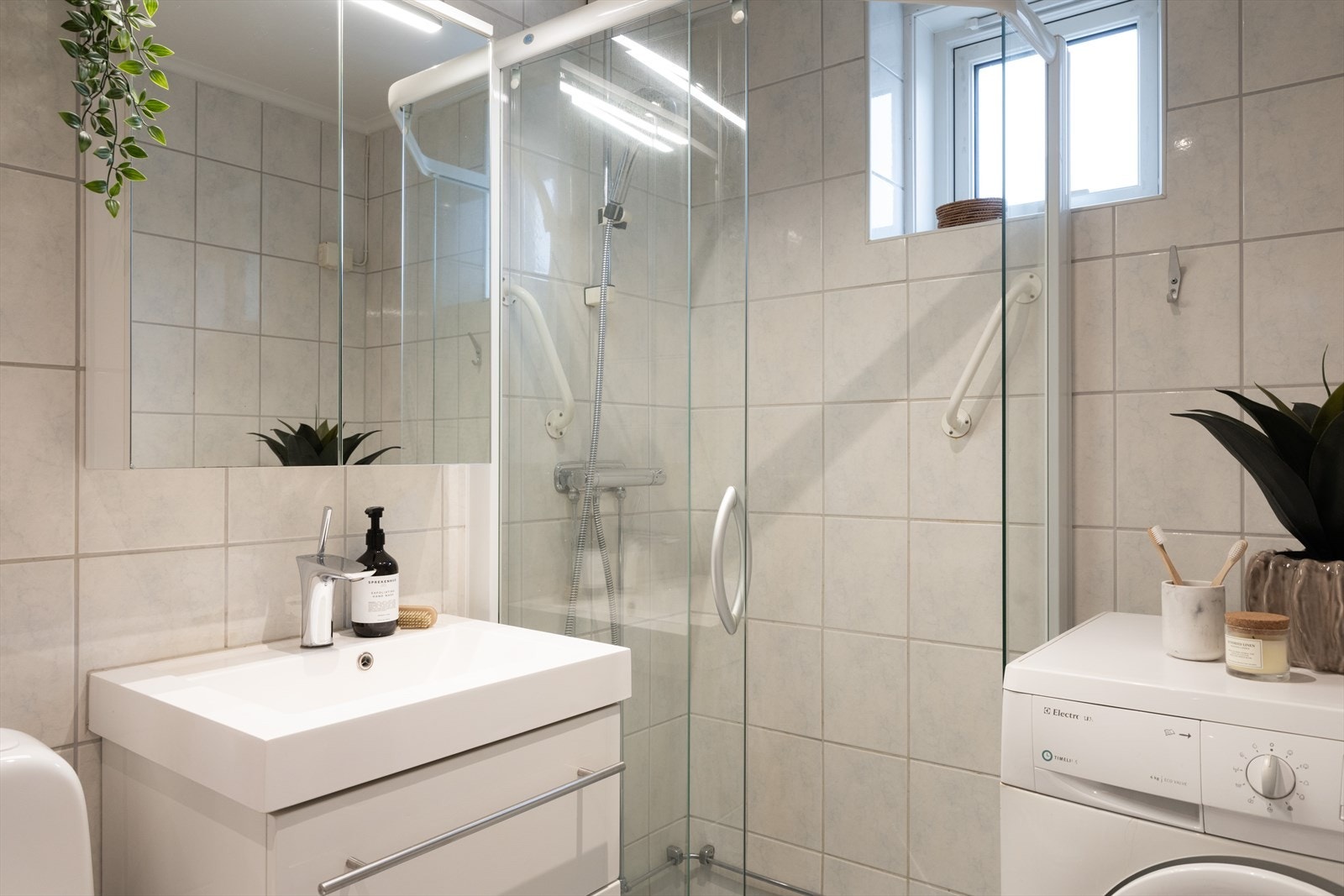 Badet er innredet med klosett, servant nedfelt i innredning, speilskap med lys og dusjhjørne med kabinettdører. Galleribilde