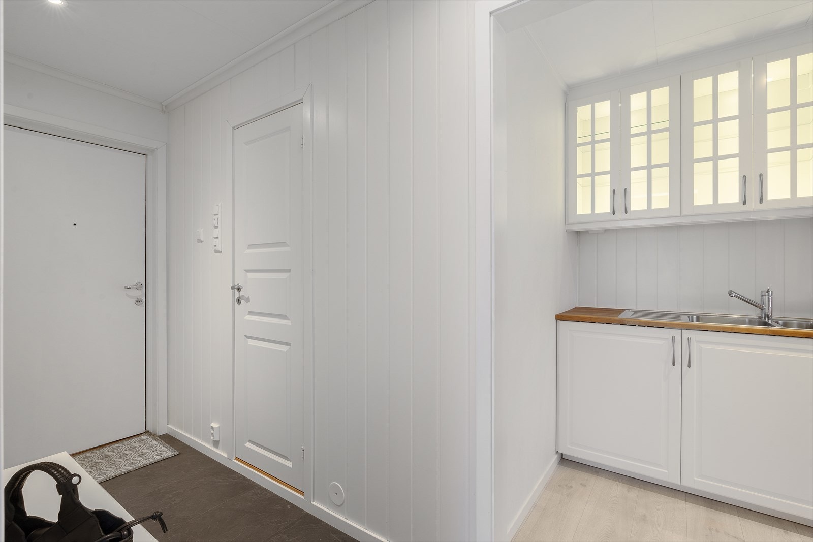 Lys entré med panelte vegger og mørke fliser på gulvet. Galleribilde