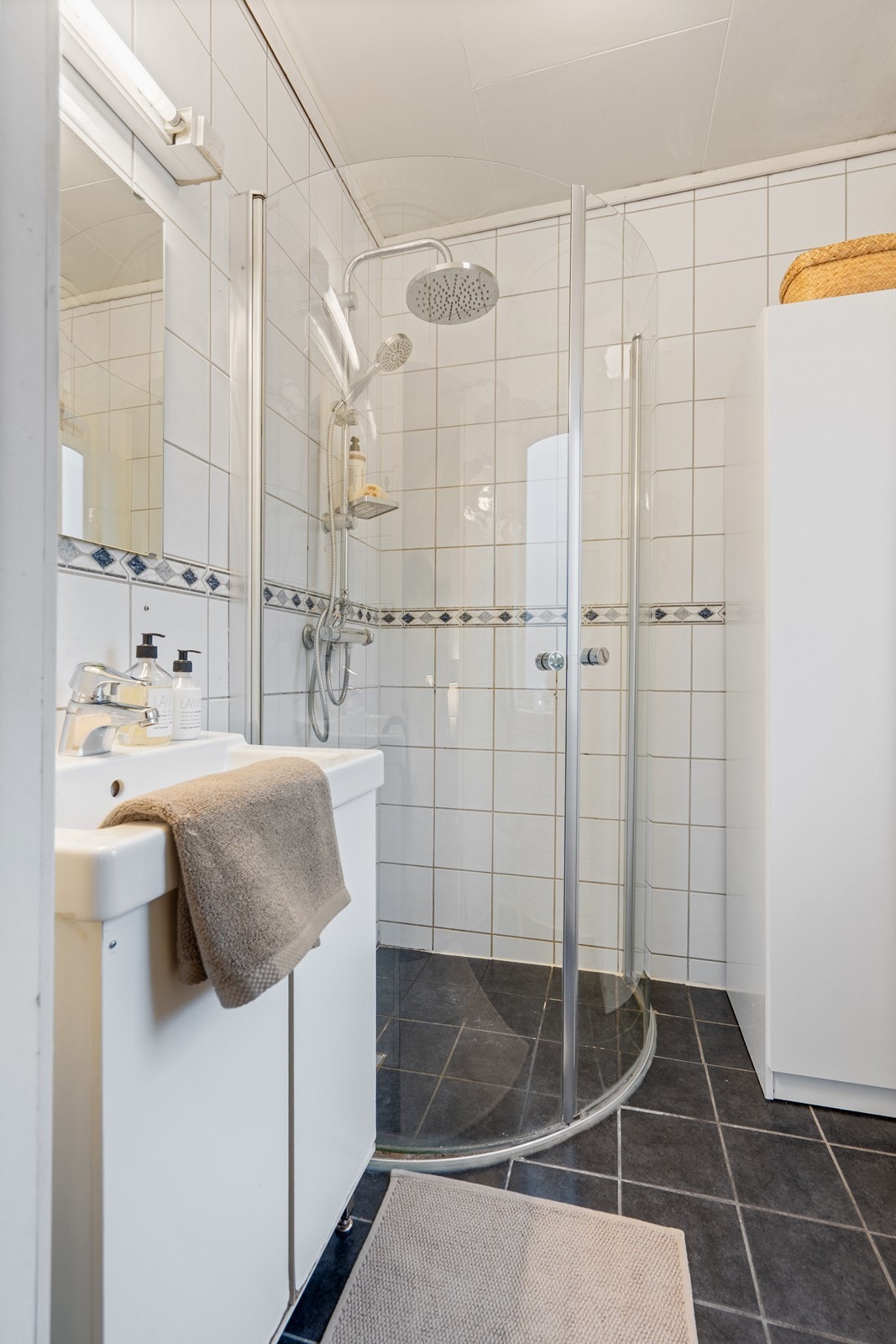 Flislagt baderom utstyrt med toalett, seksjon med servant og dusjnisje Galleribilde