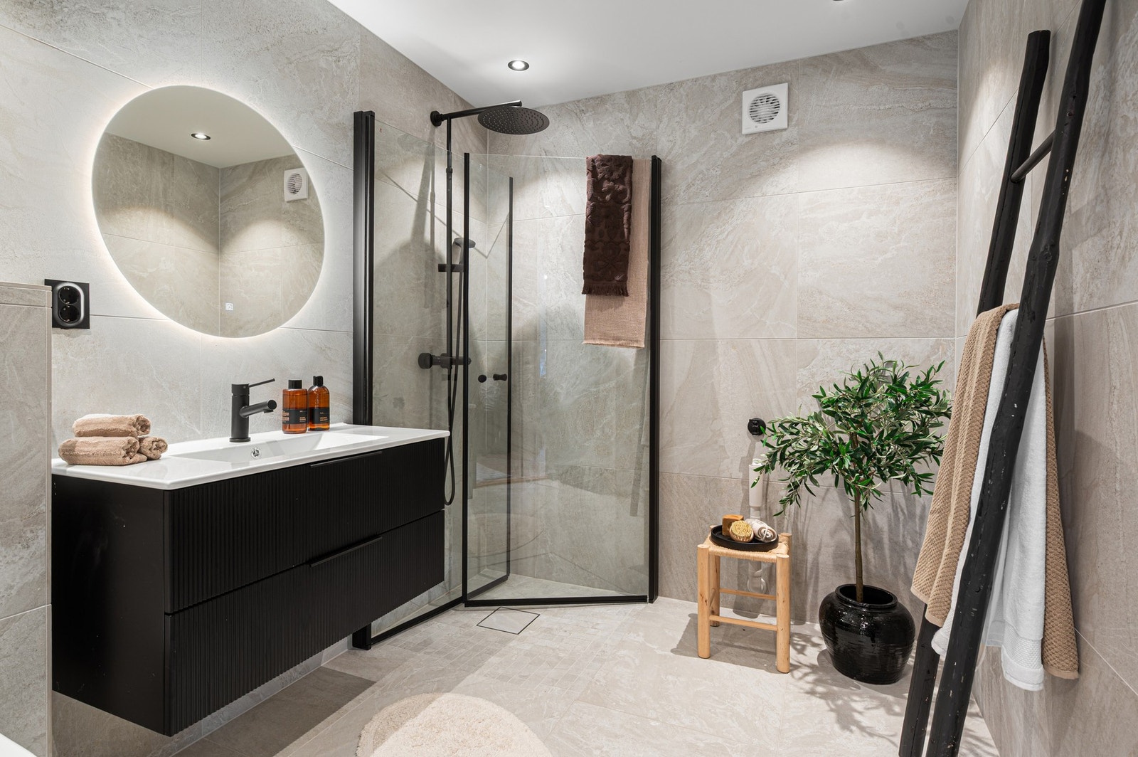 Baderommet er innredet med innfellbare og plassbesparende dusjdører i glass, rundt speil med lys, dimbare spotter i himling, kran/avløp til vaskemaskin og veggmontert WC. Galleribilde