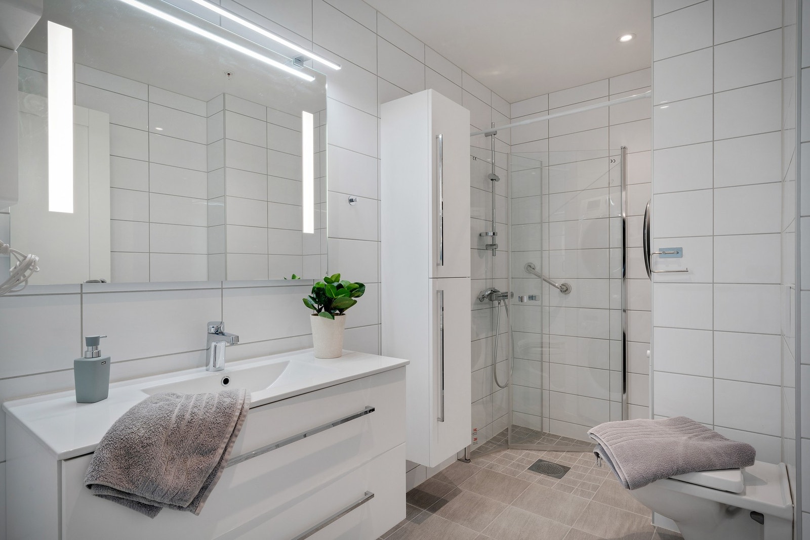 Badet er godt utstyrt med downlights, opplegg for vaskemaskin og tørketrommel, dreibare dusjvegger, vegghengt wc m.m. Galleribilde