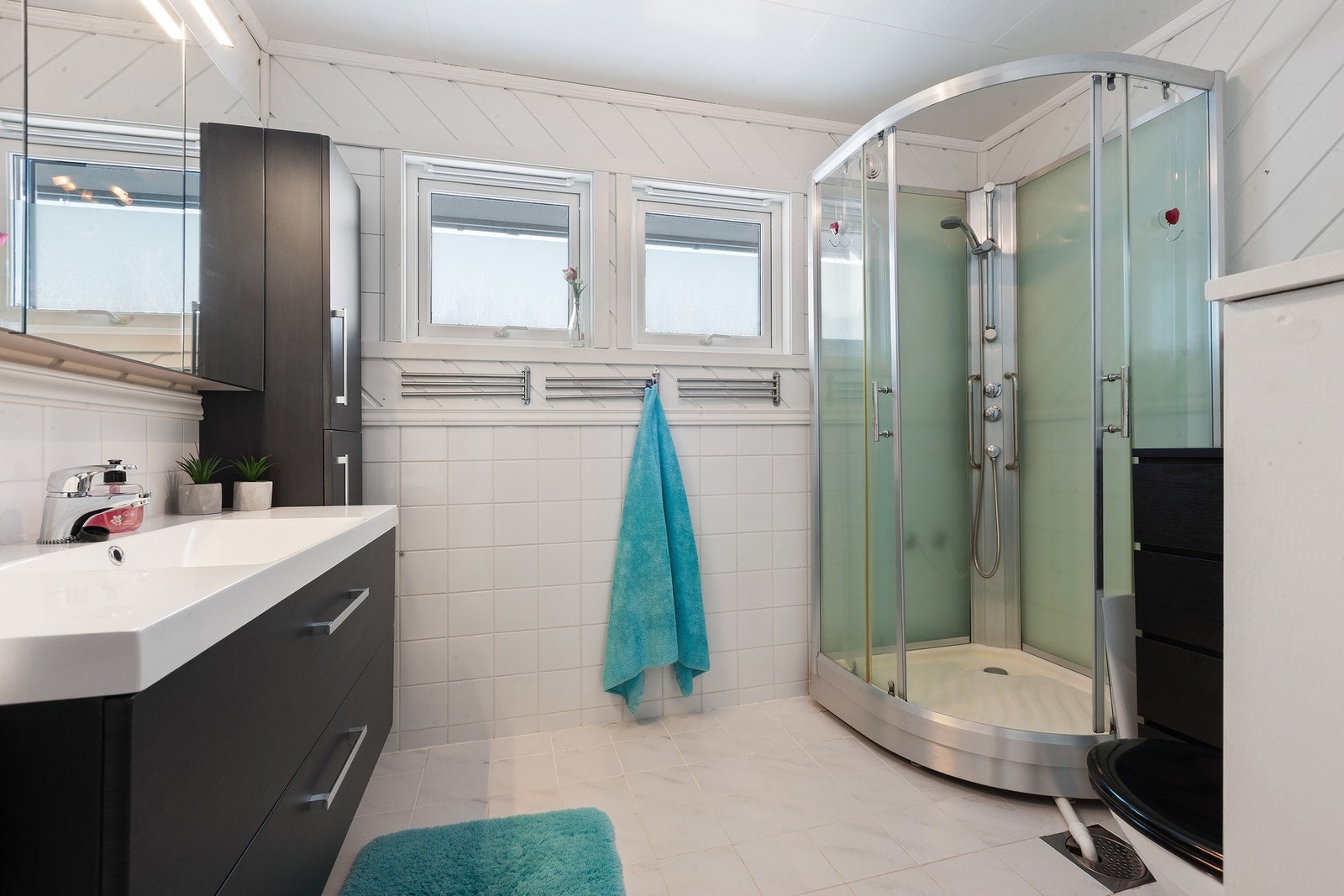 Badet har mørk innredning med slette fronter, servant med skuffer under, speiloverskap med lys over, dusjkabinett og toalett. Varme i gulv gir en fin og lun start på dagen. Galleribilde