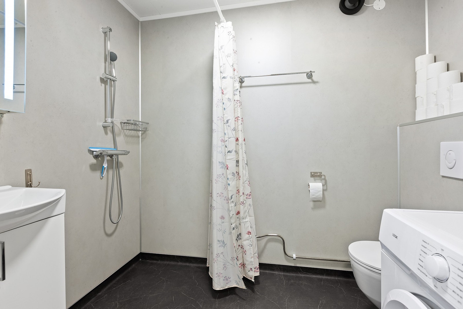 Bad med lys innredning med nedfelt servant og skap under, overskap med speil og lys over, dusj samt vegghengt toalett. Galleribilde
