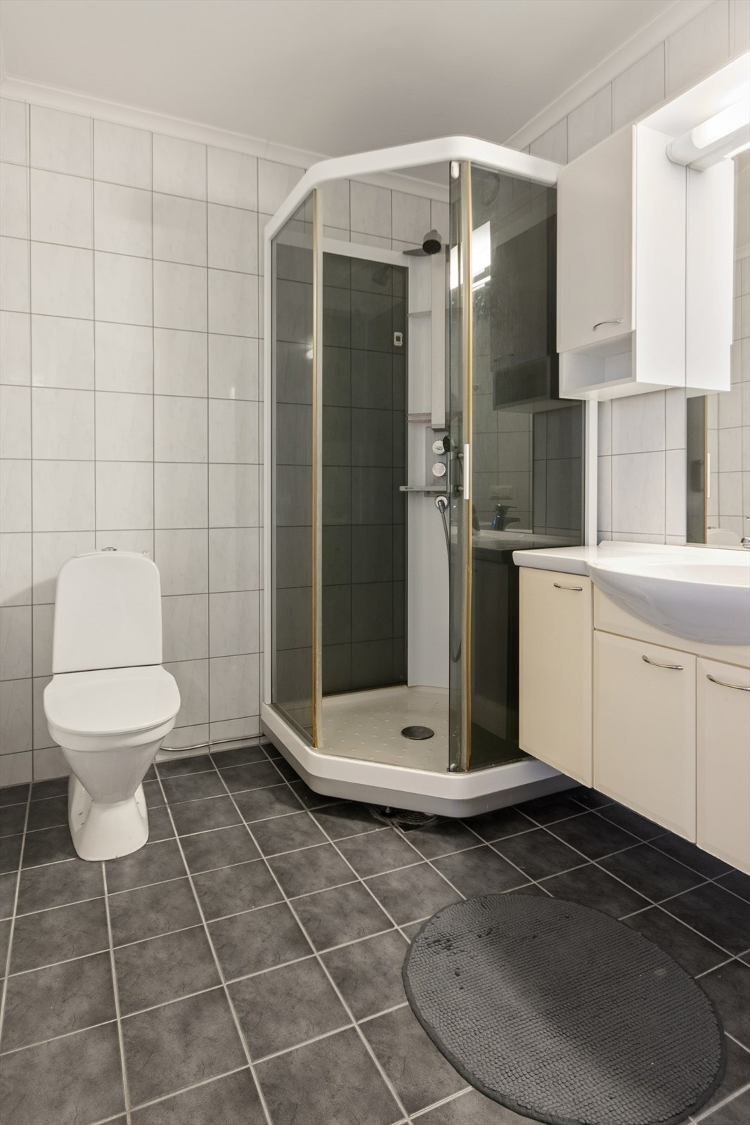Flislagt bad med pen baderomsinnredning med nedfelt servant, toalett og dusjkabinett. Galleribilde